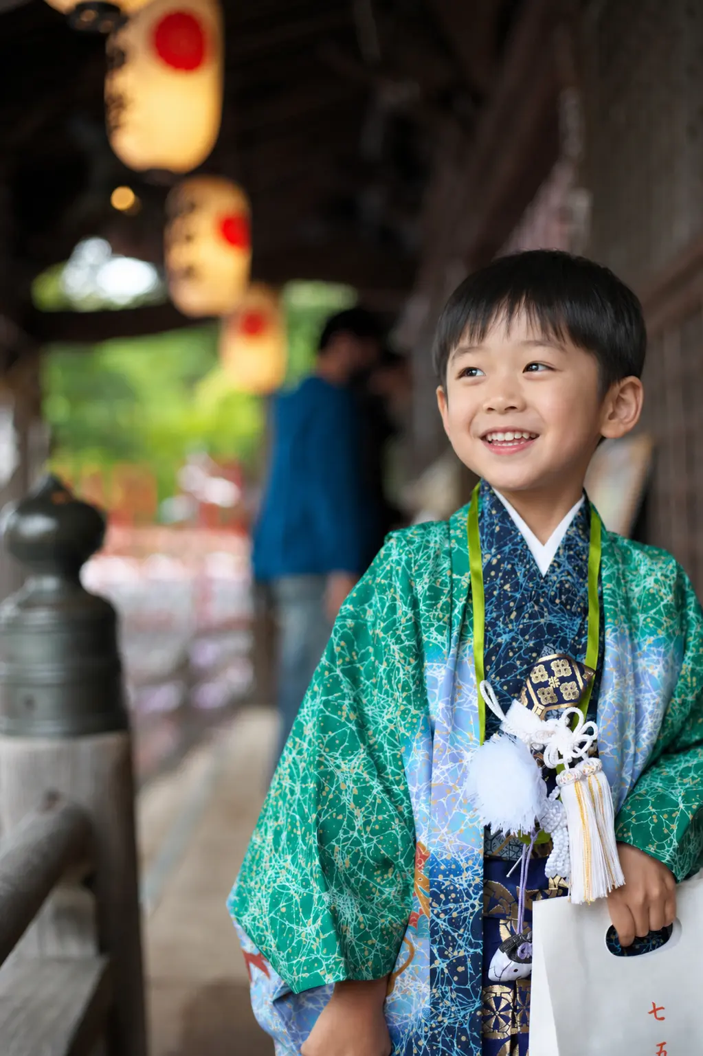 提灯の下がる回廊で見上げて笑う5歳の男の子、緑の羽織姿の七五三（石浦神社・金沢）