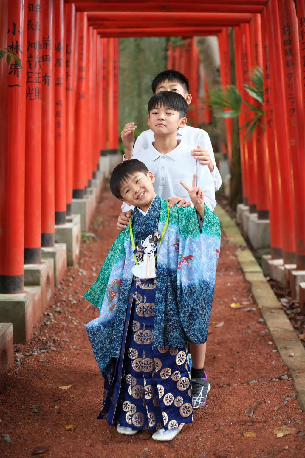 朱色の鳥居が続く石浦神社の参道に縦に並ぶ三兄弟、手前は5歳の羽織袴姿の七五三