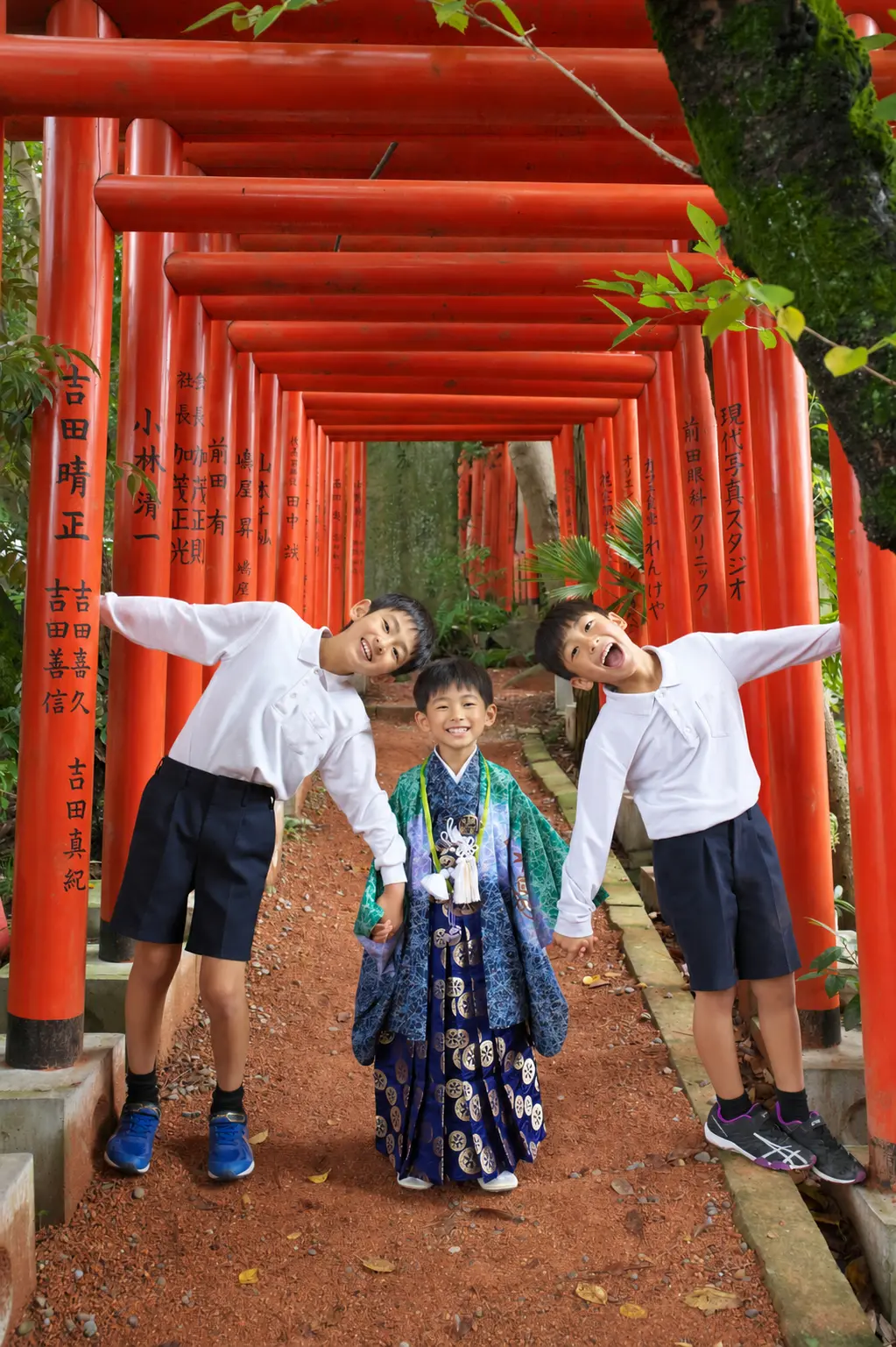 石浦神社の朱色の鳥居が連なる参道で手をつなぐ三兄弟、中央は5歳の羽織袴の七五三