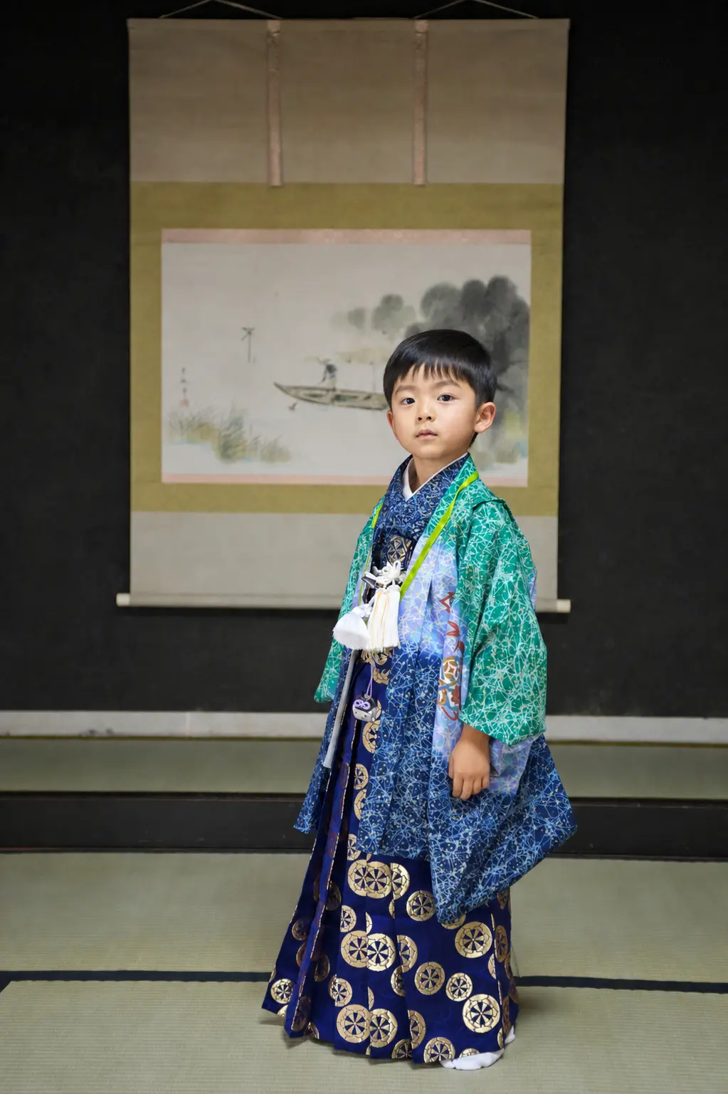 和室の掛軸を背に立つ5歳の男の子、緑の羽織と車輪柄の紺袴の七五三（金沢）
