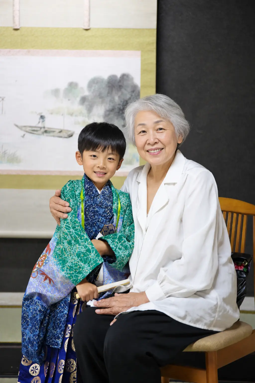 和室の掛軸前でご家族に肩を抱かれて笑う5歳の羽織袴姿の男の子、七五三の記念写真