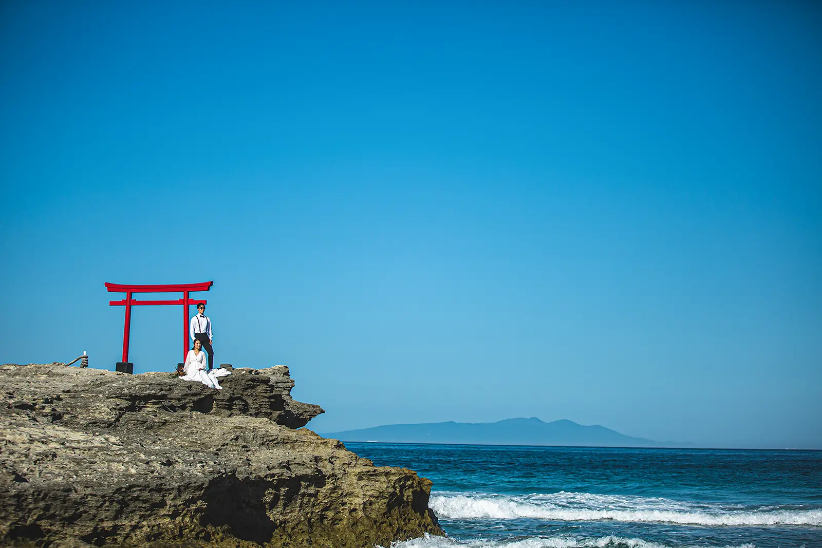 伊豆白浜の海辺で赤い鳥居と海を背景に撮影する新郎新婦