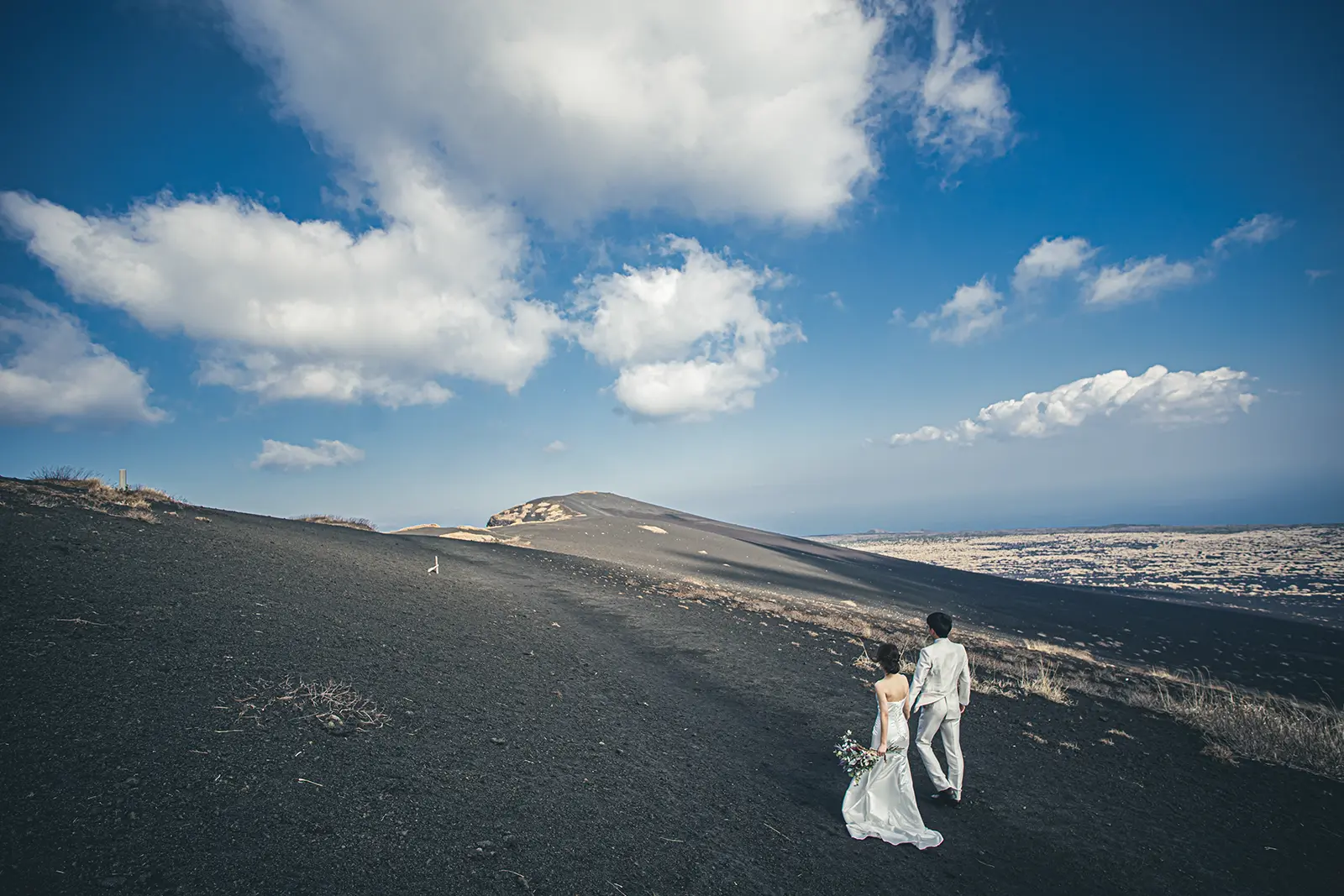 伊豆大島・三原山の黒い大地で撮るフォトウェディング alt:伊豆大島の三原山の黒い大地を歩く新郎新婦の後ろ姿