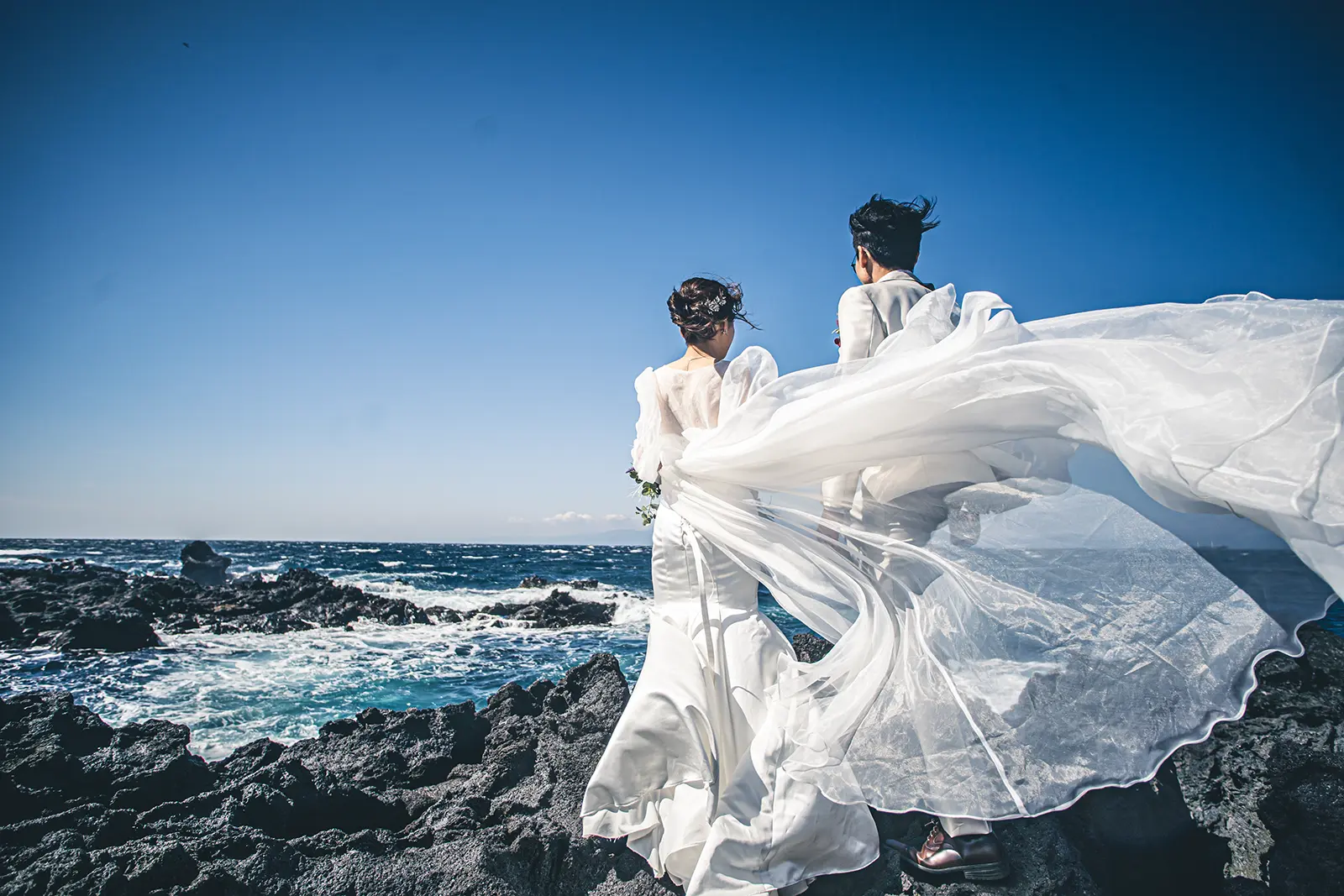 伊豆大島の海辺で風になびくベールと新郎新婦を撮影したフォトウェディング写真