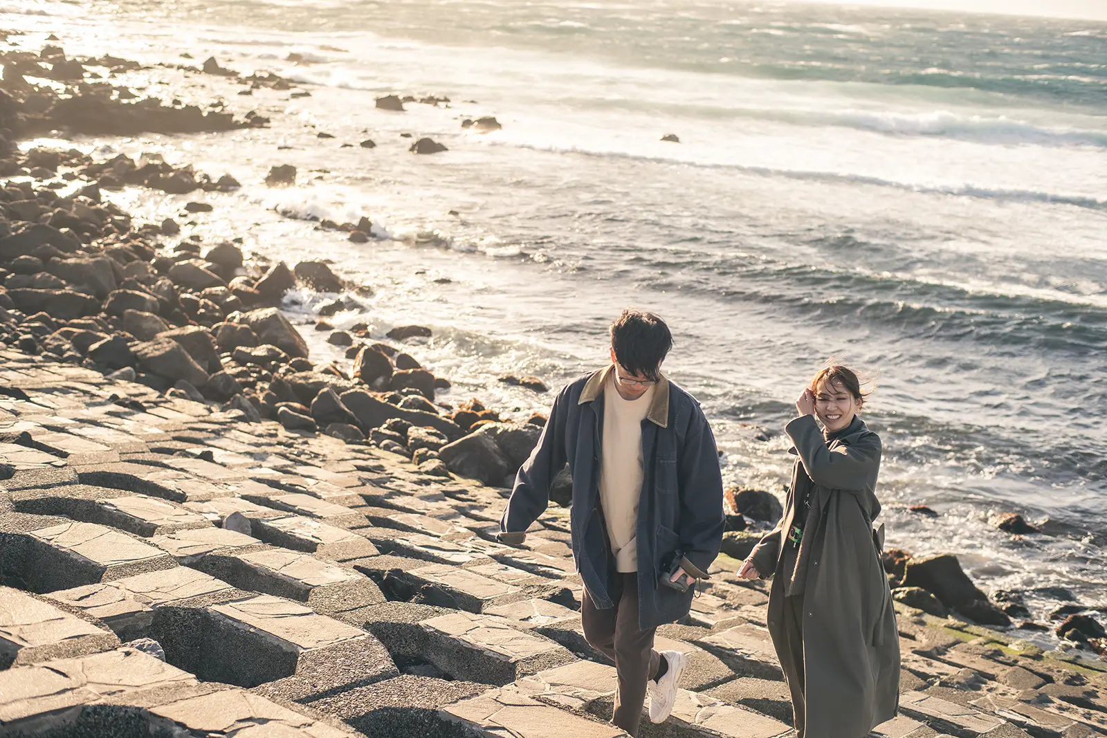 伊豆大島の海沿いの岩場を歩くカップルの旅フォト