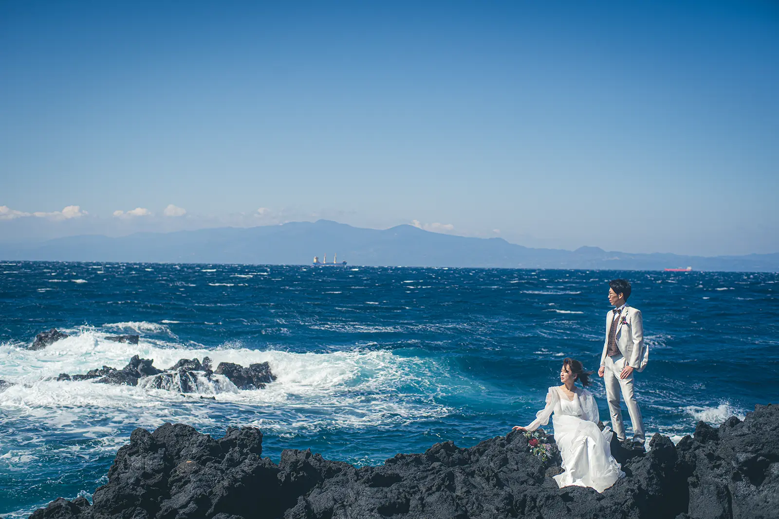 伊豆大島の青い海と岩場を背景にした新郎新婦のフォトウェディング写真