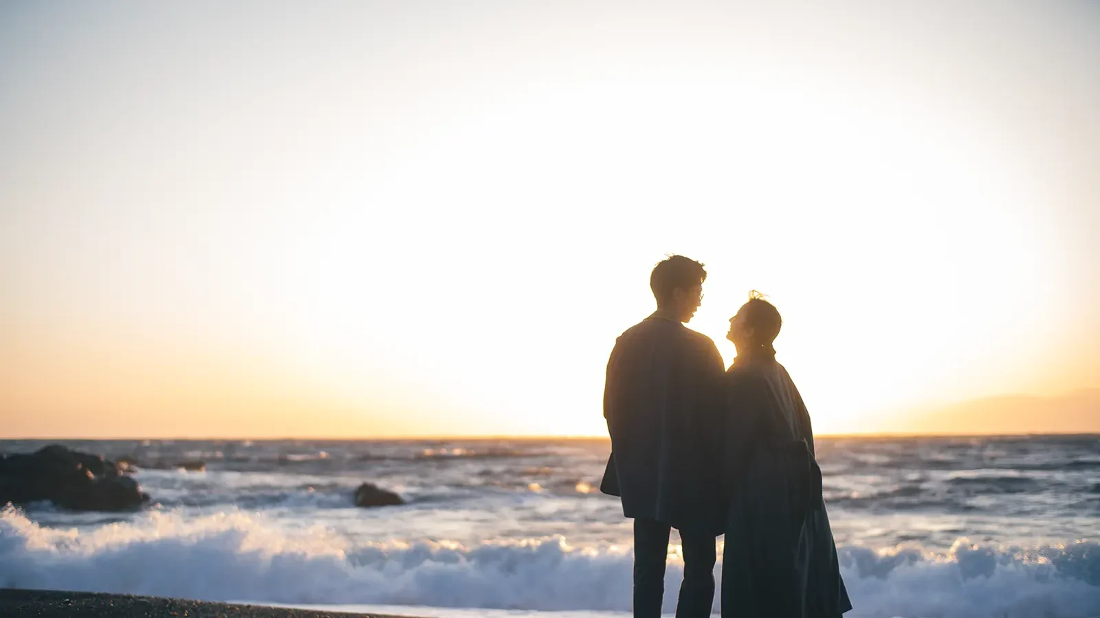 伊豆大島の夕日に照らされた海を見つめるカップルのシルエット写真