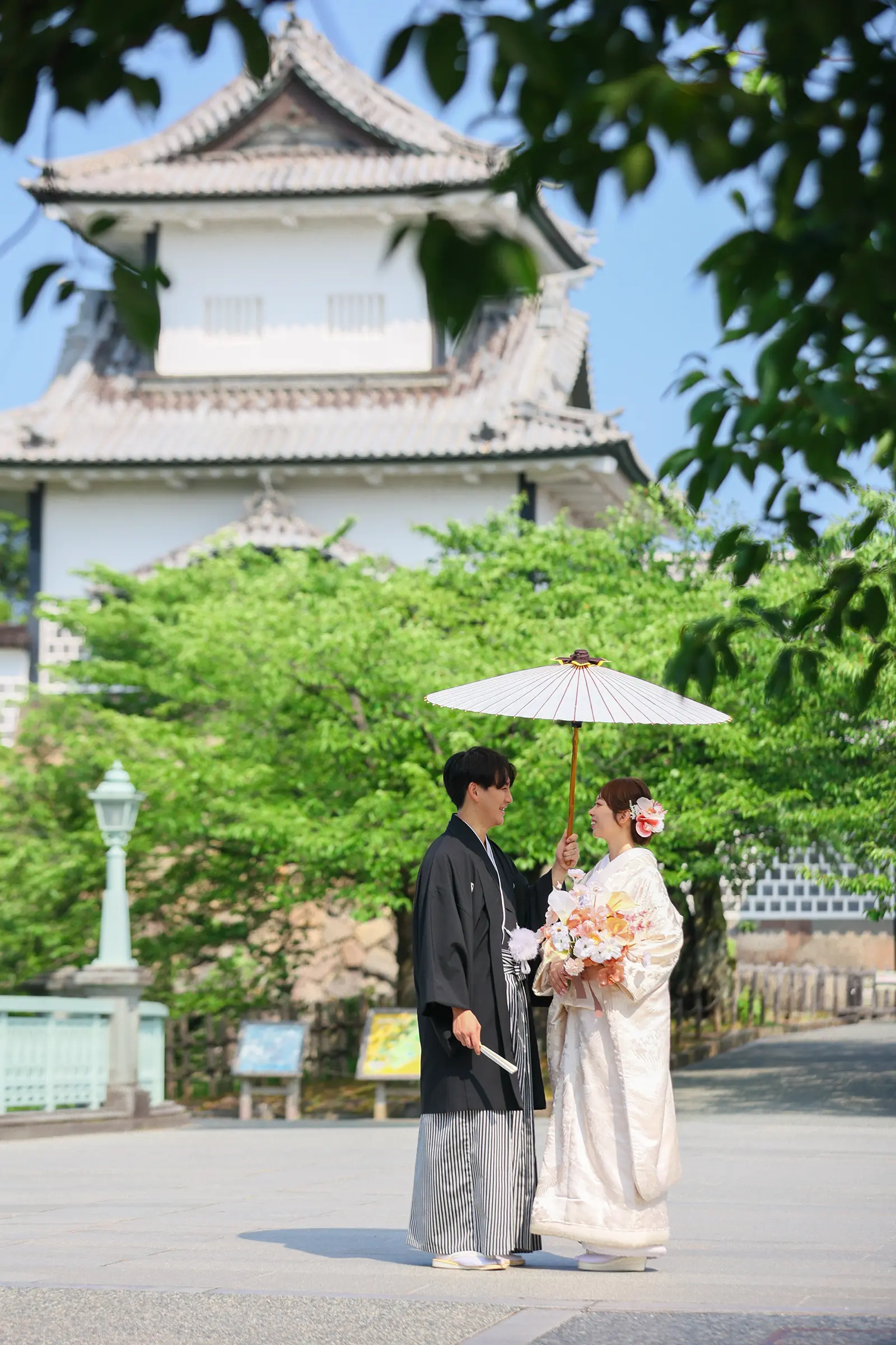 金沢城を背景に和傘を持って向かい合う和装姿の新郎新婦