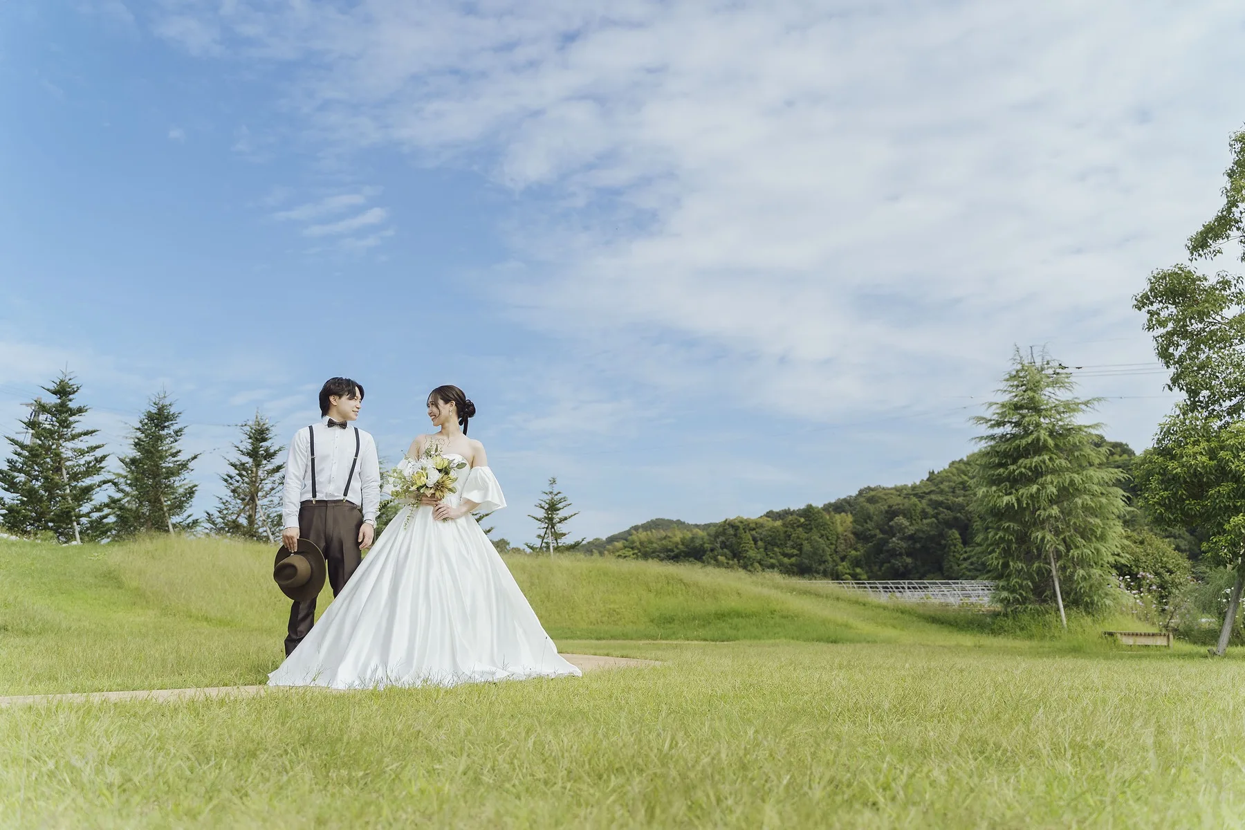金沢のぶどうの森のガーデンを歩くウエディングドレスの新婦とサスペンダー姿の新郎