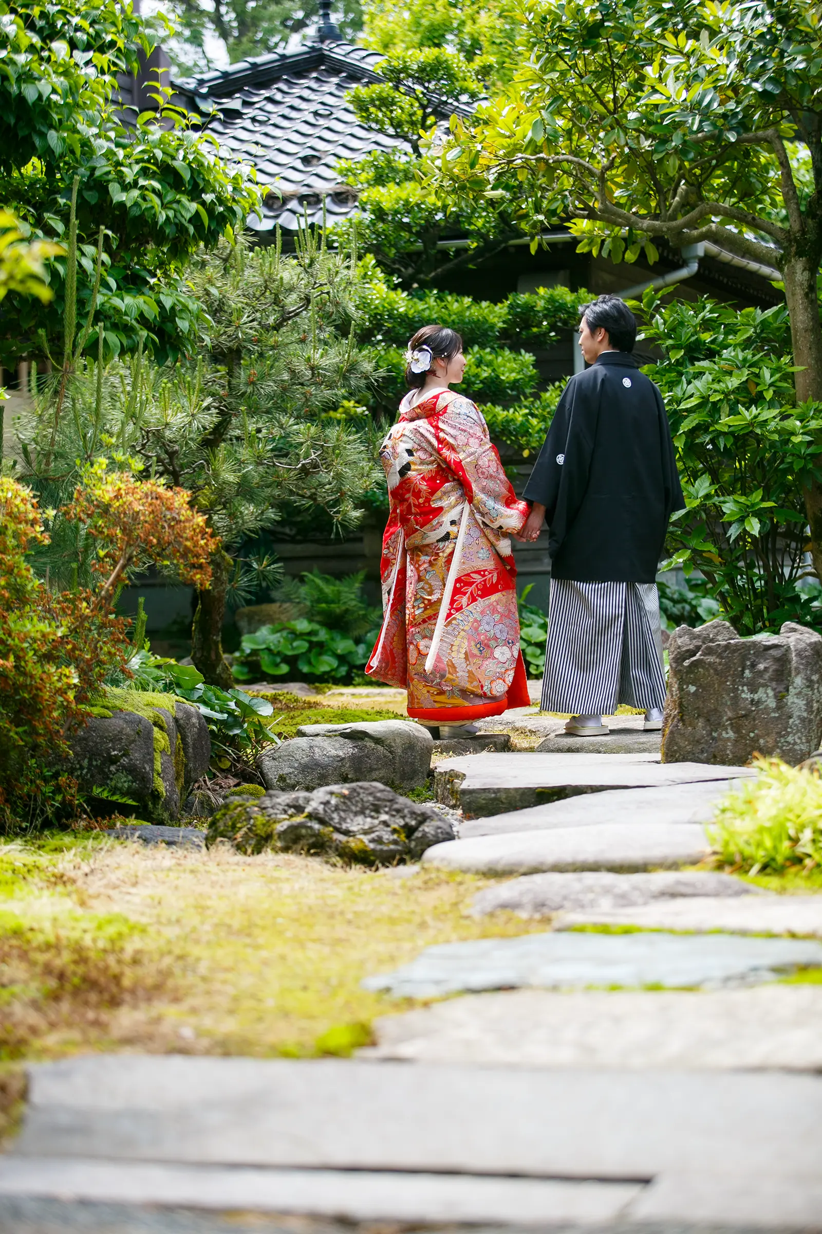 松任ふるさと館の日本庭園で色打掛の花嫁と紋付袴の新郎が振り返る和装前撮り写真