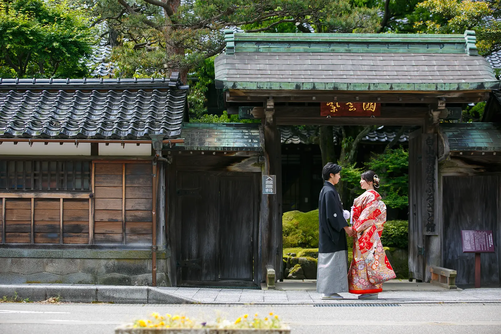 松任ふるさと館の門前で赤い色打掛の花嫁と紋付袴の新郎が向かい合う和装前撮り