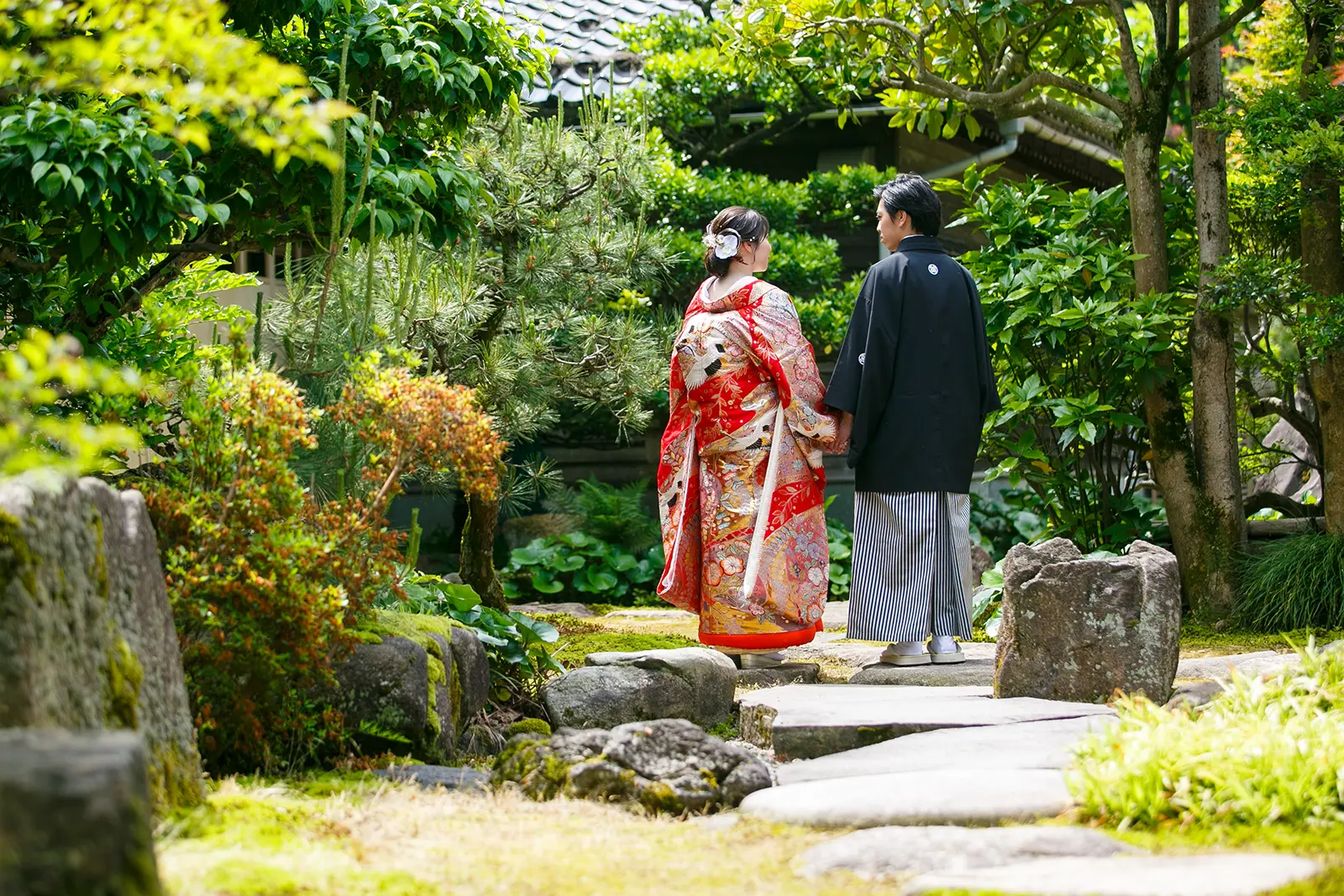 松任ふるさと館の日本庭園で色打掛の花嫁と紋付袴の新郎が手をつないで歩く前撮り写真