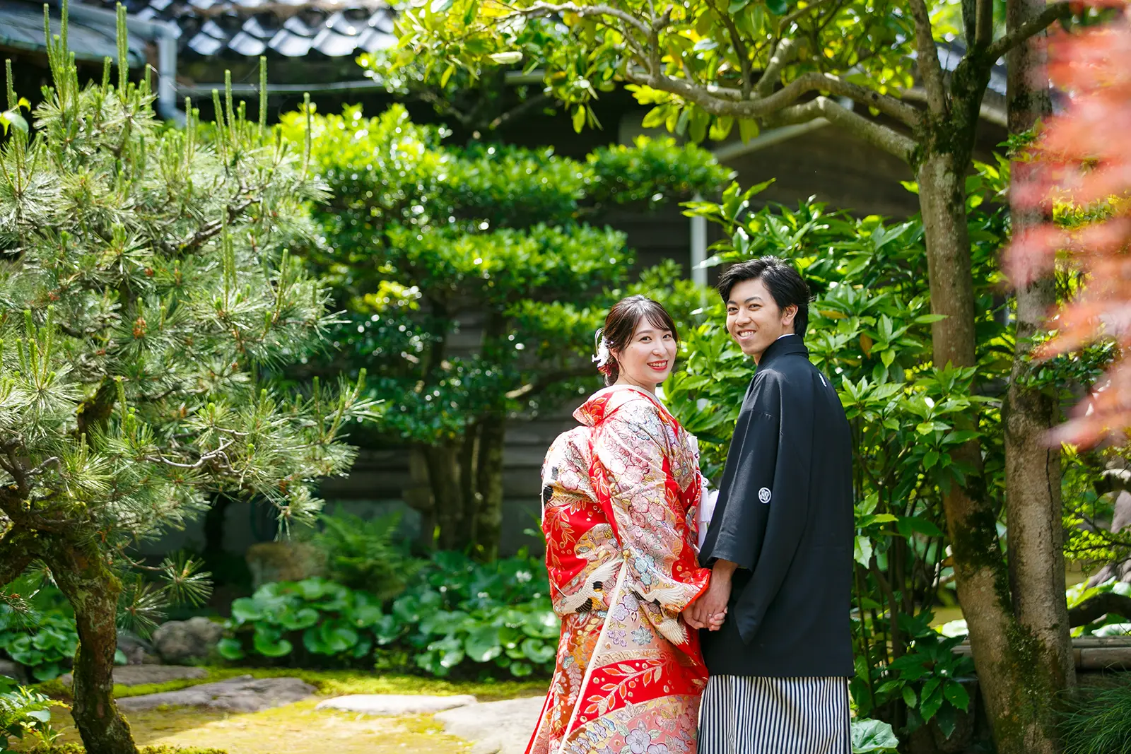 松任ふるさと館の日本庭園で赤い和傘を持つ色打掛の花嫁と紋付袴の新郎