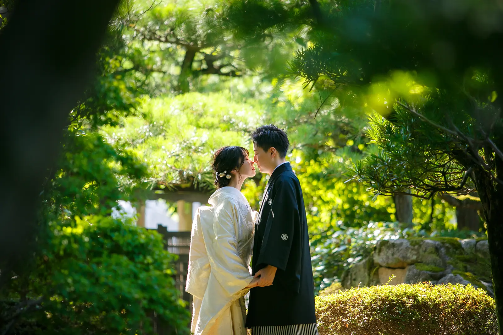 松任ふるさと館の日本庭園で白無垢の花嫁と紋付袴の新郎が木漏れ日の中で向かい合う前撮り写真