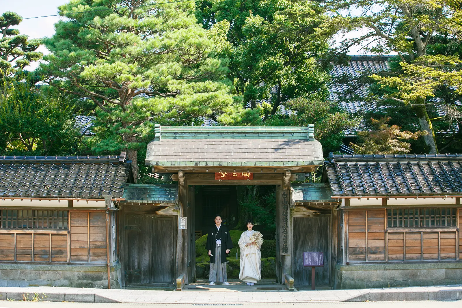 松任ふるさと館の大きな門構えを背景に白無垢と紋付袴のお二人が立つ和装前撮り