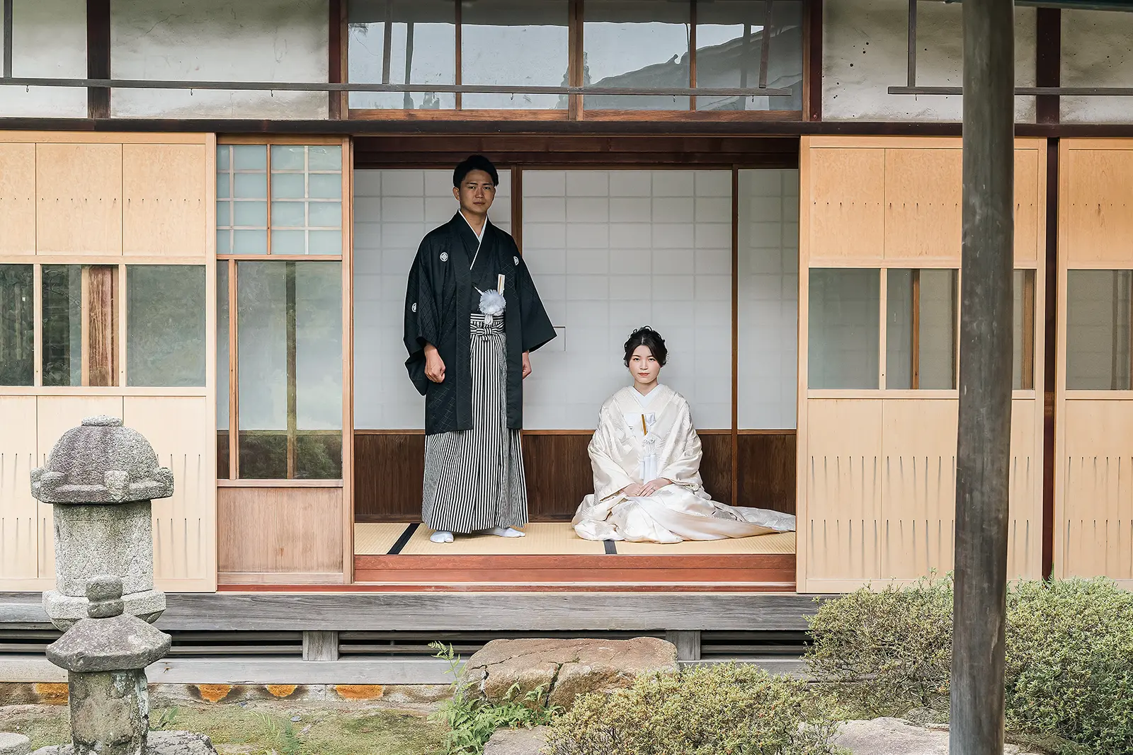 松任ふるさと館の縁側で白無垢の花嫁が座り紋付袴の新郎が立つ和装前撮り