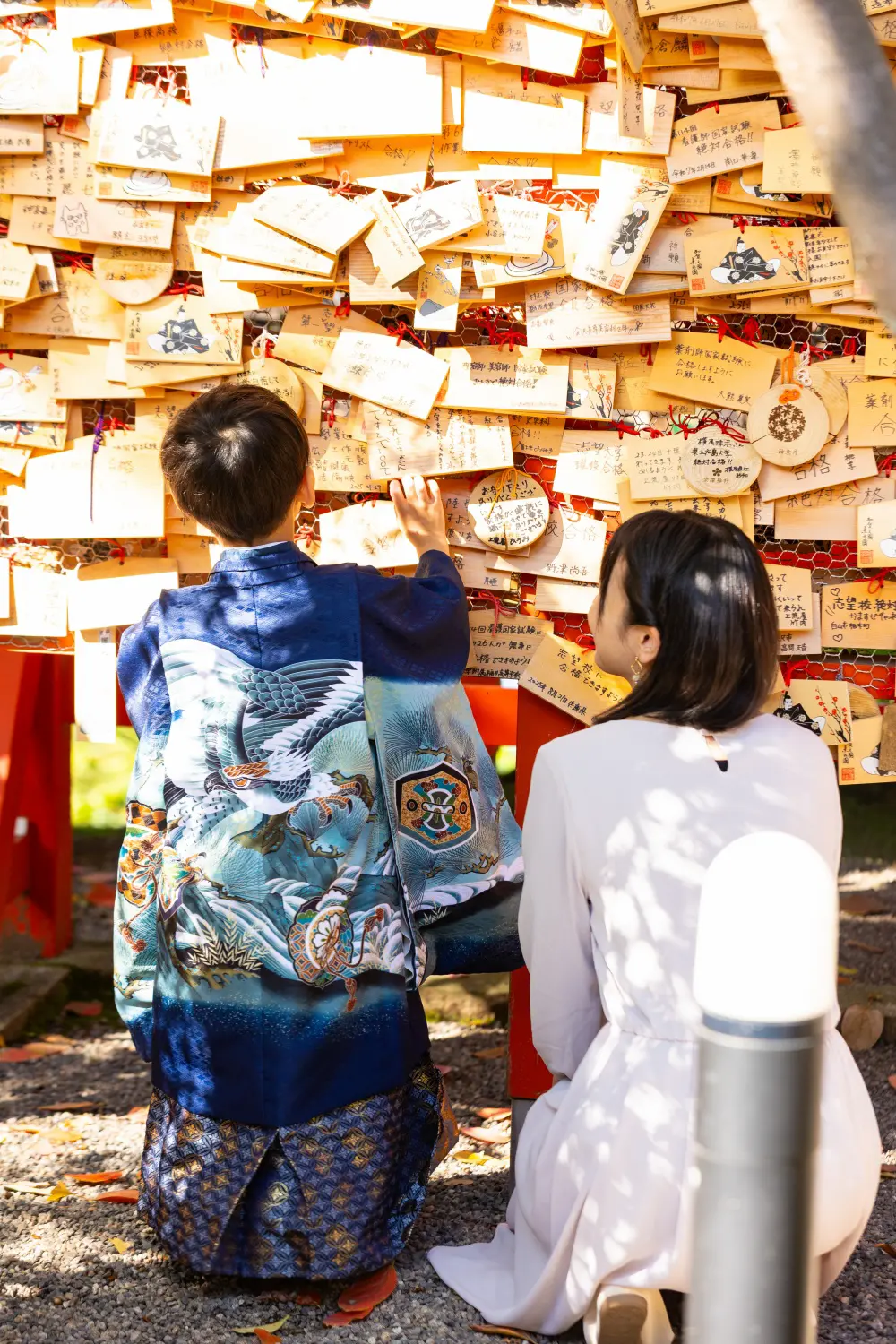 絵馬がびっしり掛かった棚の前で母としゃがんで見上げる5歳の男の子の後ろ姿、七五三（金澤神社・金沢）