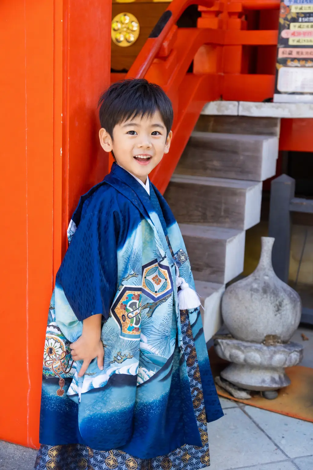 金澤神社の朱塗りの柱にもたれて笑う5歳の男の子、濃紺から水色にぼかした羽織袴の七五三出張撮影（金沢）