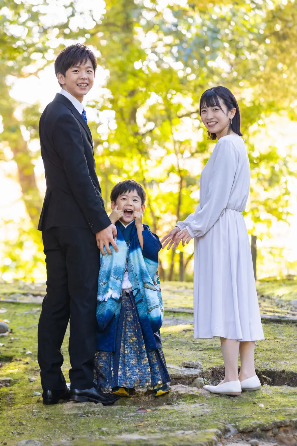 黄葉しかけた木立の中で振り返って笑う羽織袴の5歳の男の子とご両親、七五三（金澤神社・金沢）