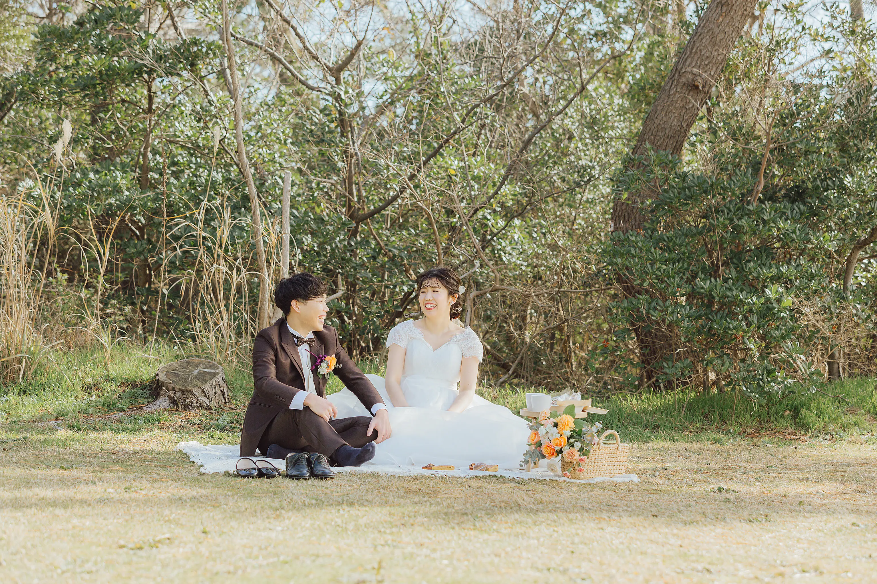 金沢・健民海浜公園の芝生でピクニックシートに座り笑い合う新郎新婦とブーケや小物
