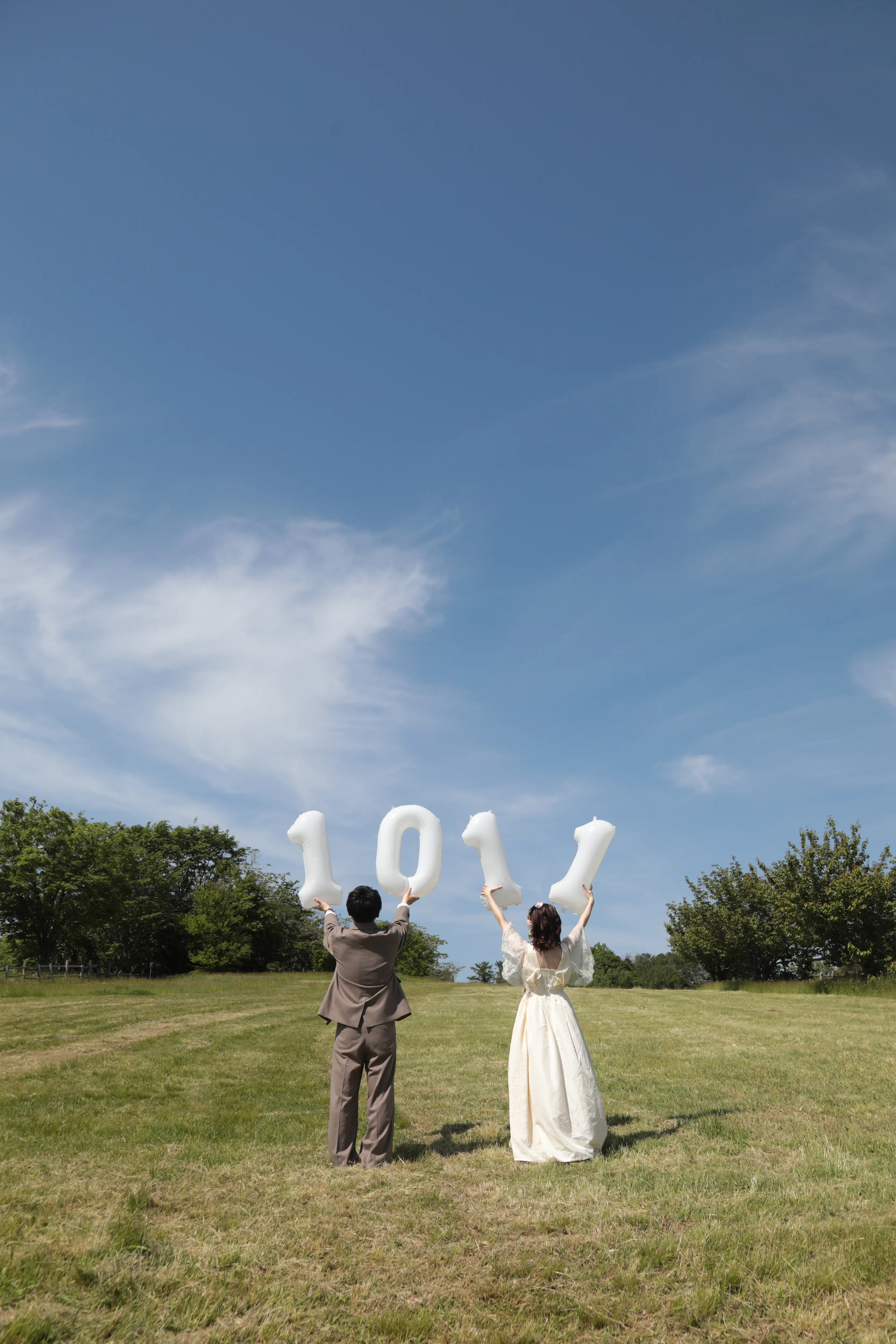 金沢のキゴ山で青空に向かってLOVEのレターバルーンを掲げる洋装の新郎新婦の後ろ姿