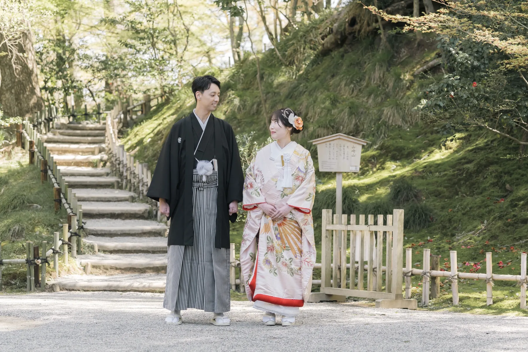 竹垣と石段のある庭園の小径を並んで歩く、黒紋付袴の新郎と色打掛の花嫁｜金沢の和装ロケーションフォトウェディング