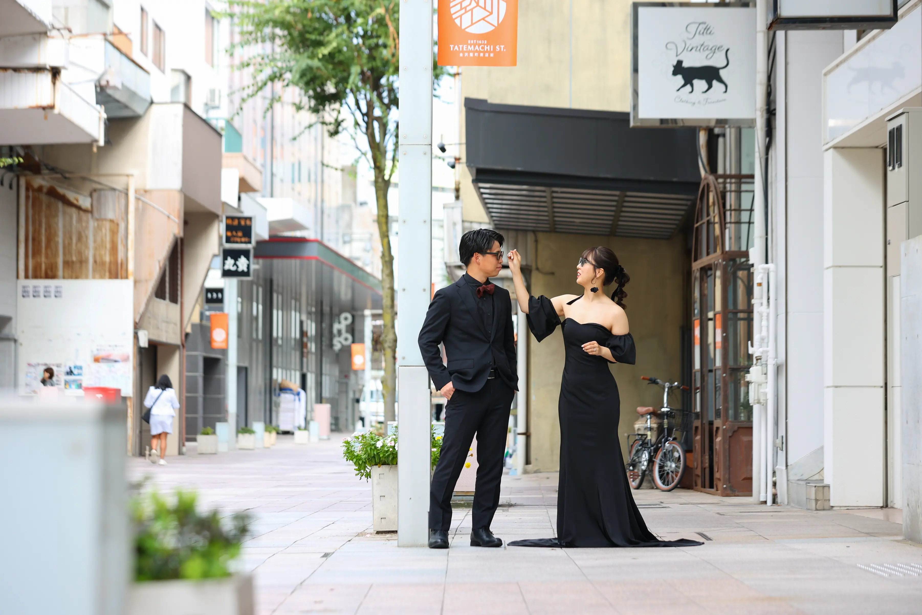 金沢・竪町の商店街で新郎の手を取りポーズをとる黒いオフショルダードレスの新婦と黒いスーツの新郎