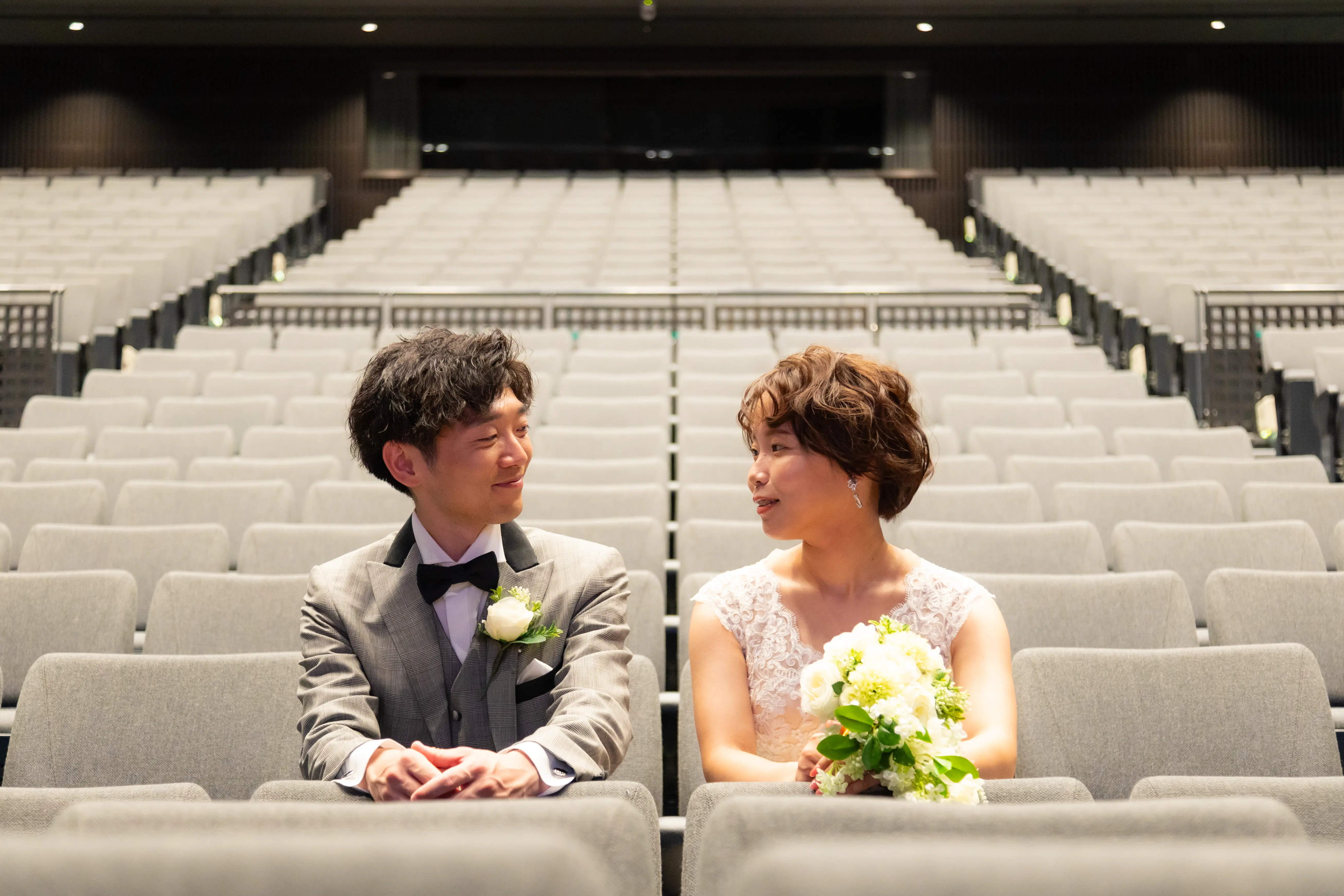 能登演劇堂の客席に並んで座り笑顔で見つめ合う新郎新婦