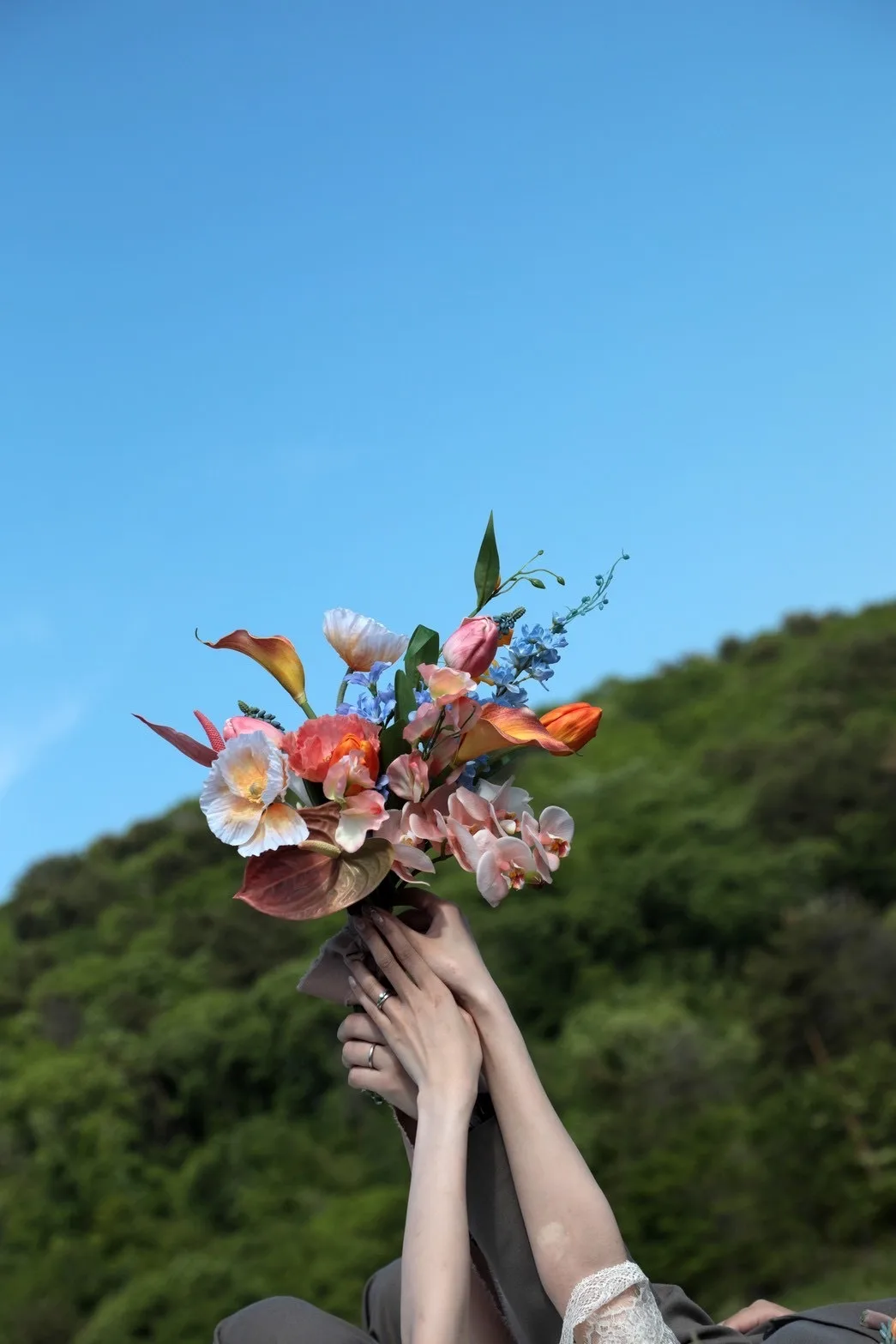 青空を背景に手作りのオリジナルブーケを掲げる花嫁の手元|金沢のフォトウェディング