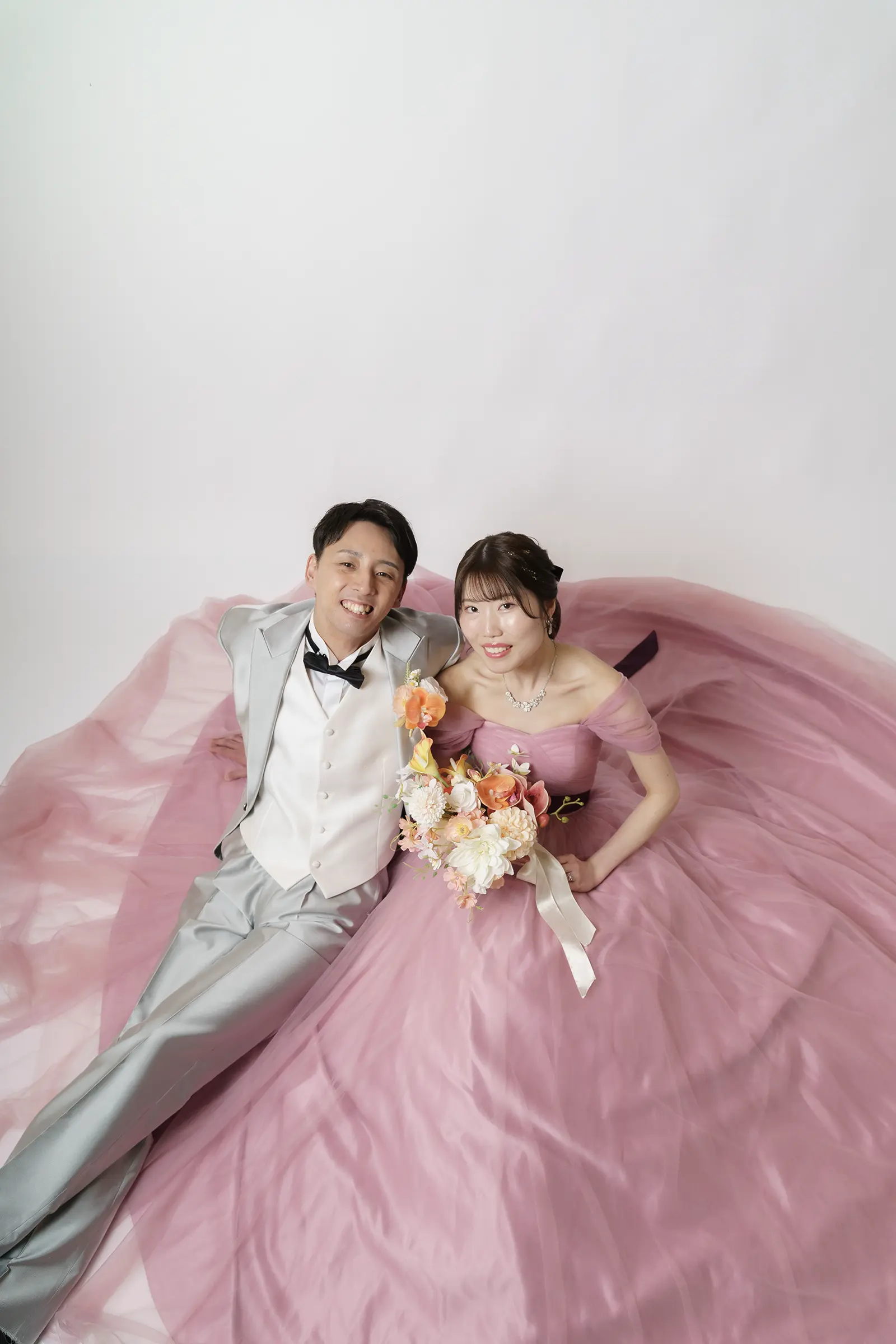 ピンクのカラードレス姿の花嫁と新郎が座って見上げるスタジオ写真
