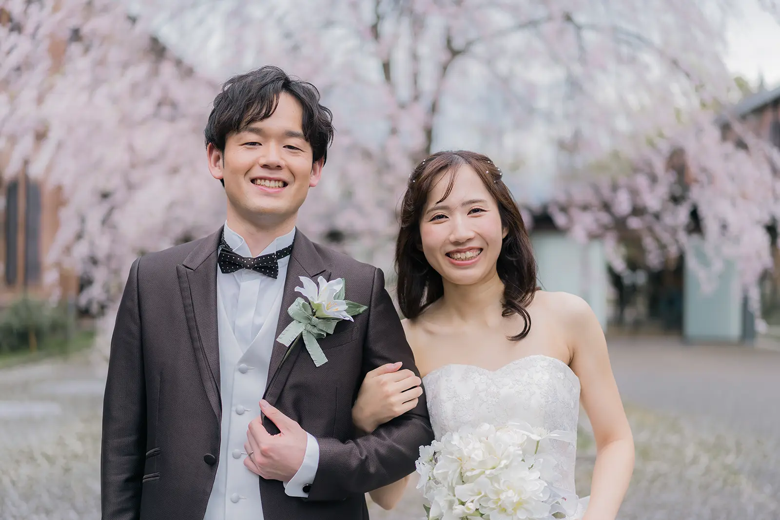 桜を背景に笑顔で並ぶ洋装姿の新郎新婦