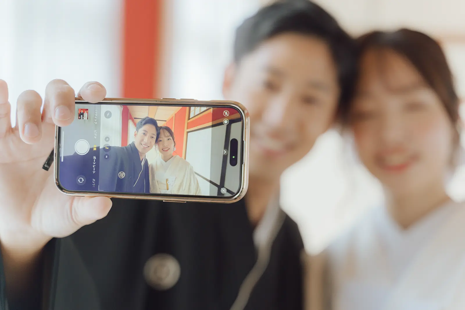 スマートフォン越しに和装姿の新郎新婦を写した前撮り写真
