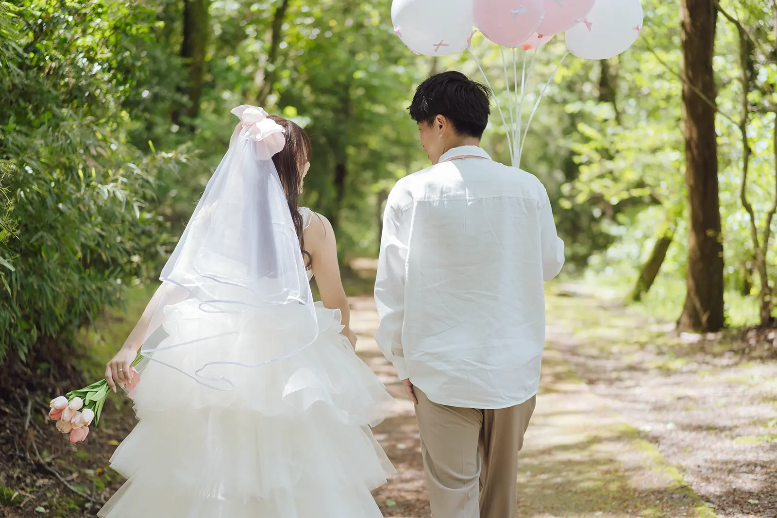 緑の小道を歩く洋装姿の新郎新婦の後ろ姿