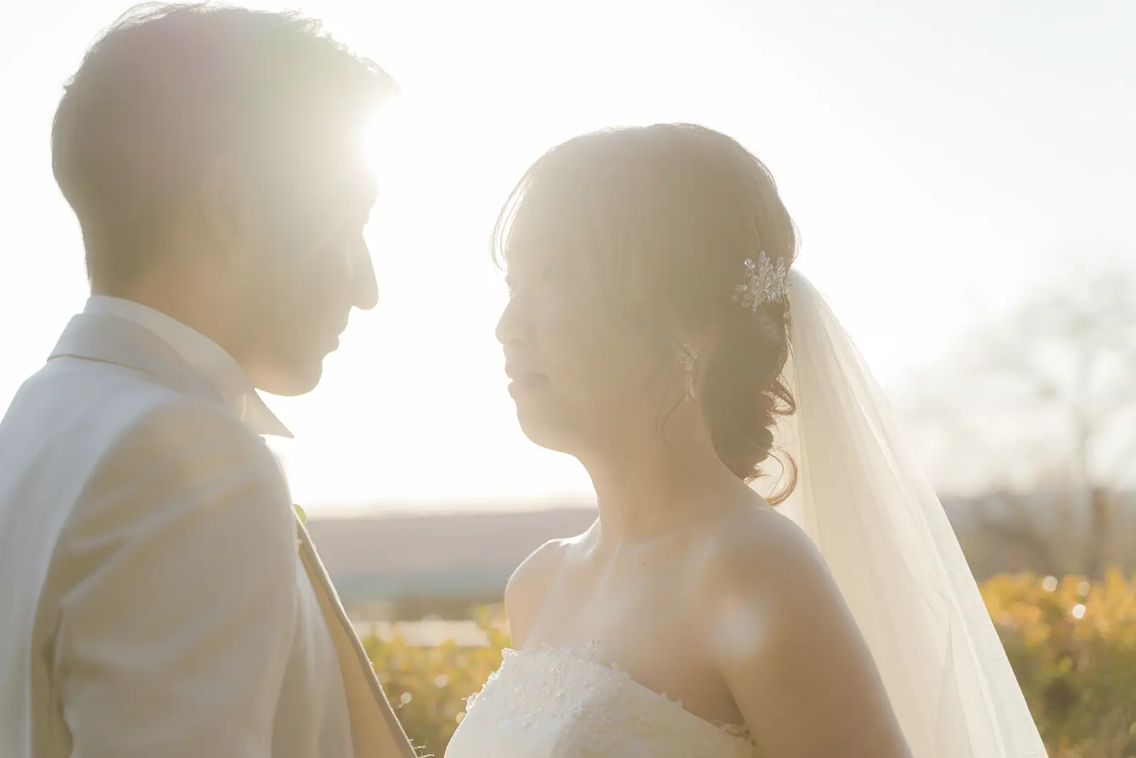 夕景の光の中で向かい合う洋装姿の新郎新婦のシルエット写真
