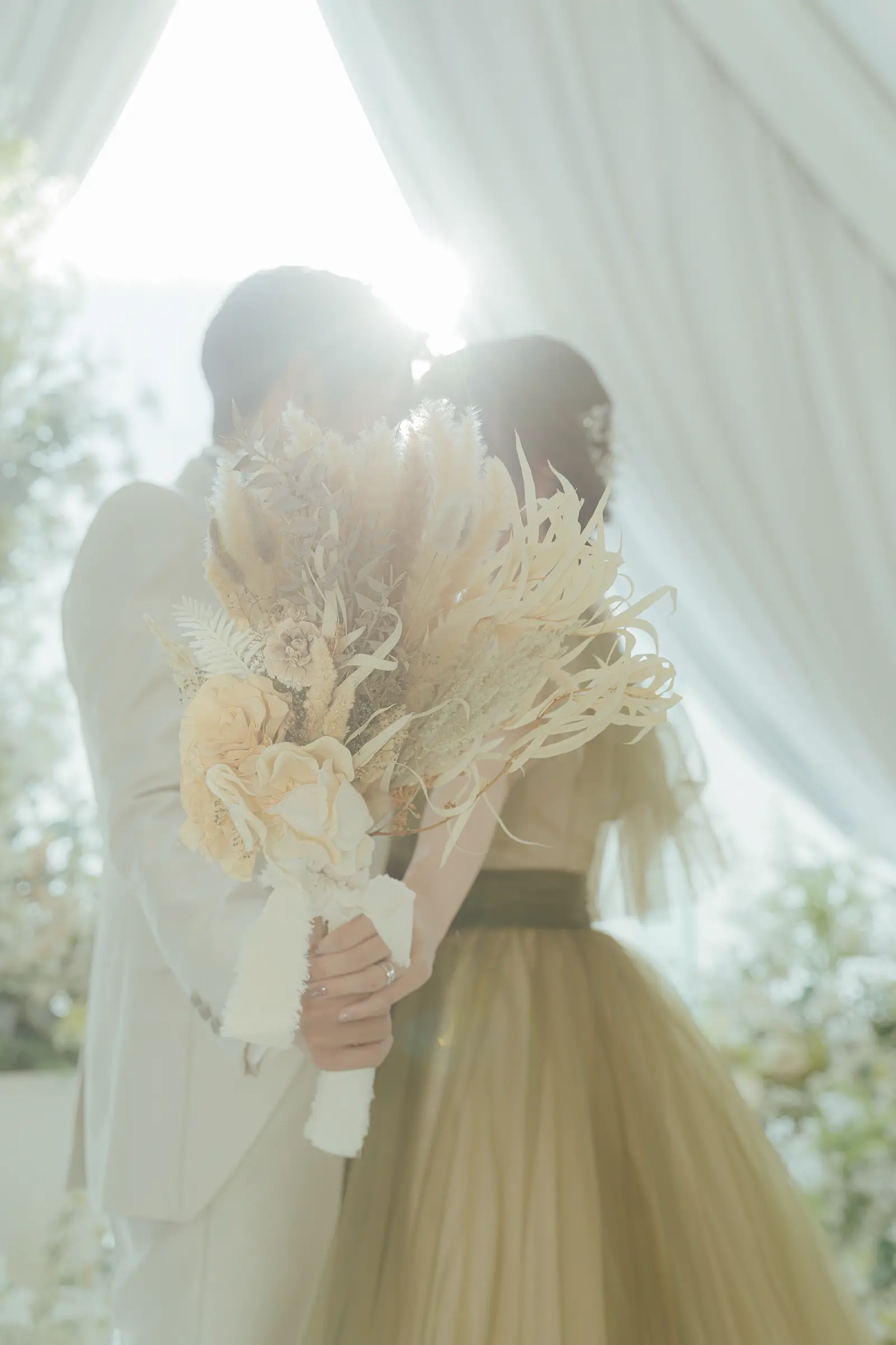 ベールとブーケ越しに向かい合う洋装姿の新郎新婦
