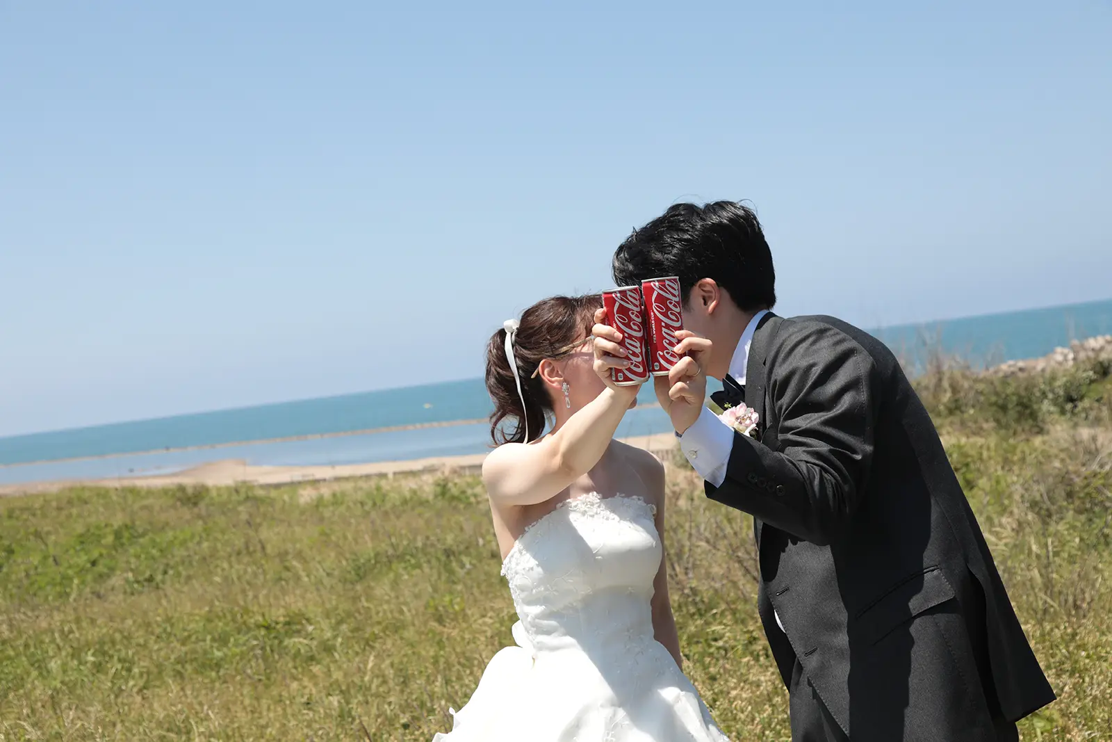 海辺でコーラ缶を持ちながら向き合う新郎新婦