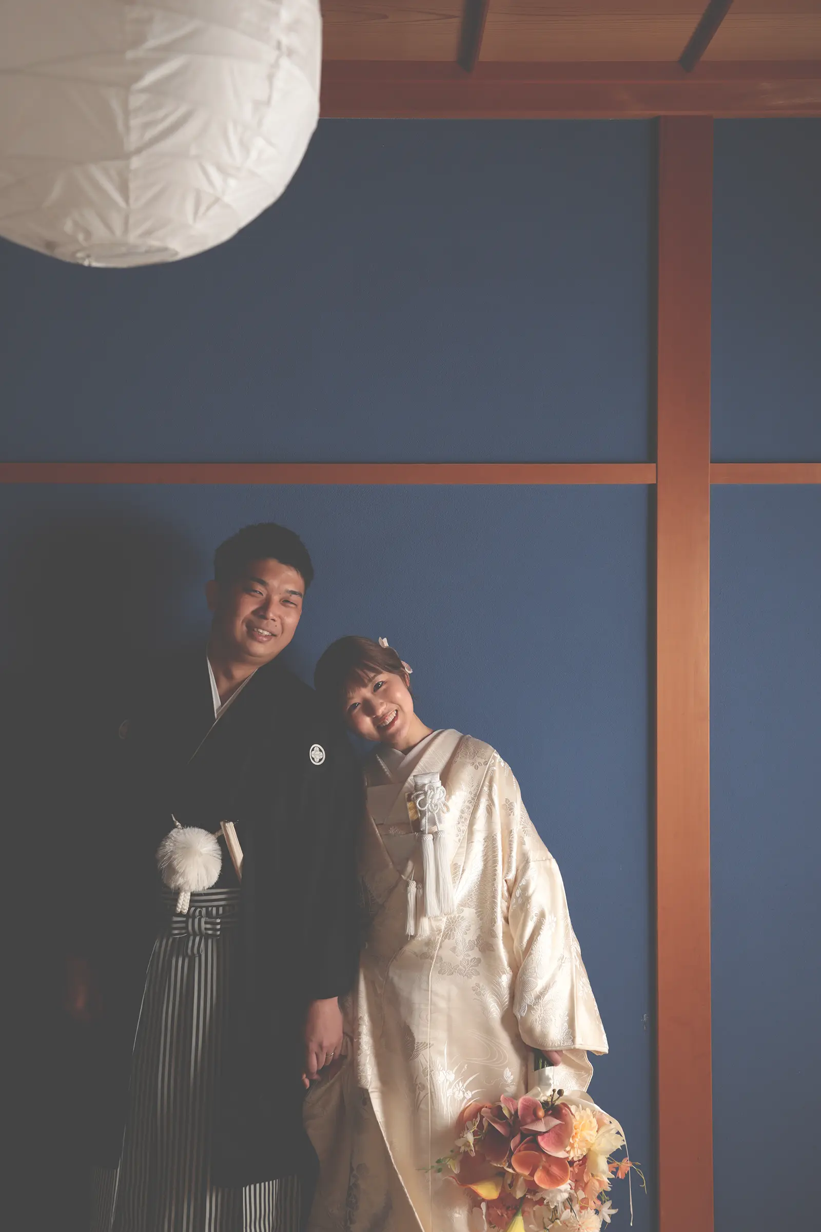 青い和室で寄り添いながら笑う和装の新郎新婦