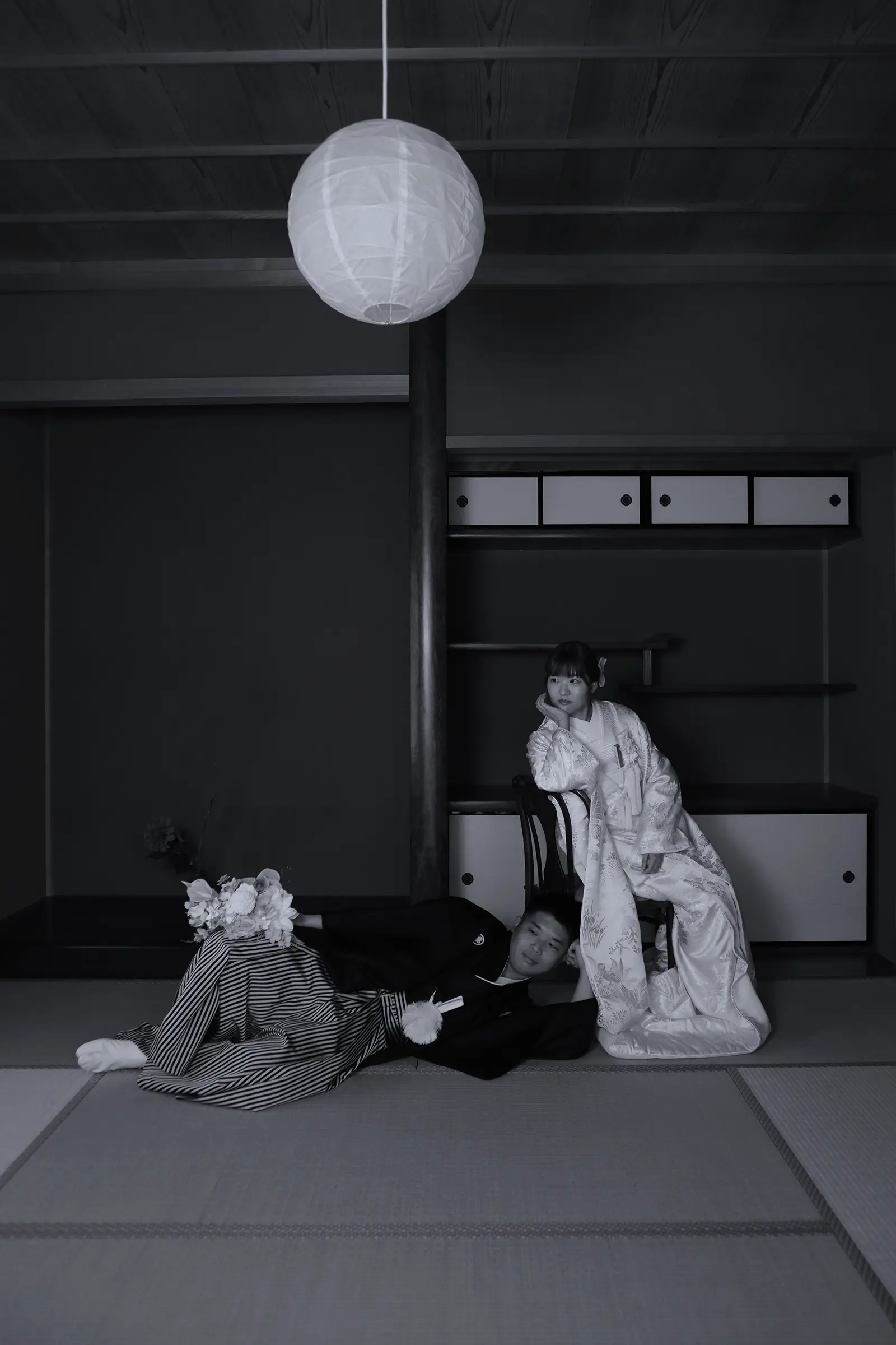 青い和室で遊び心あるポーズをする新郎新婦のモノクロ写真