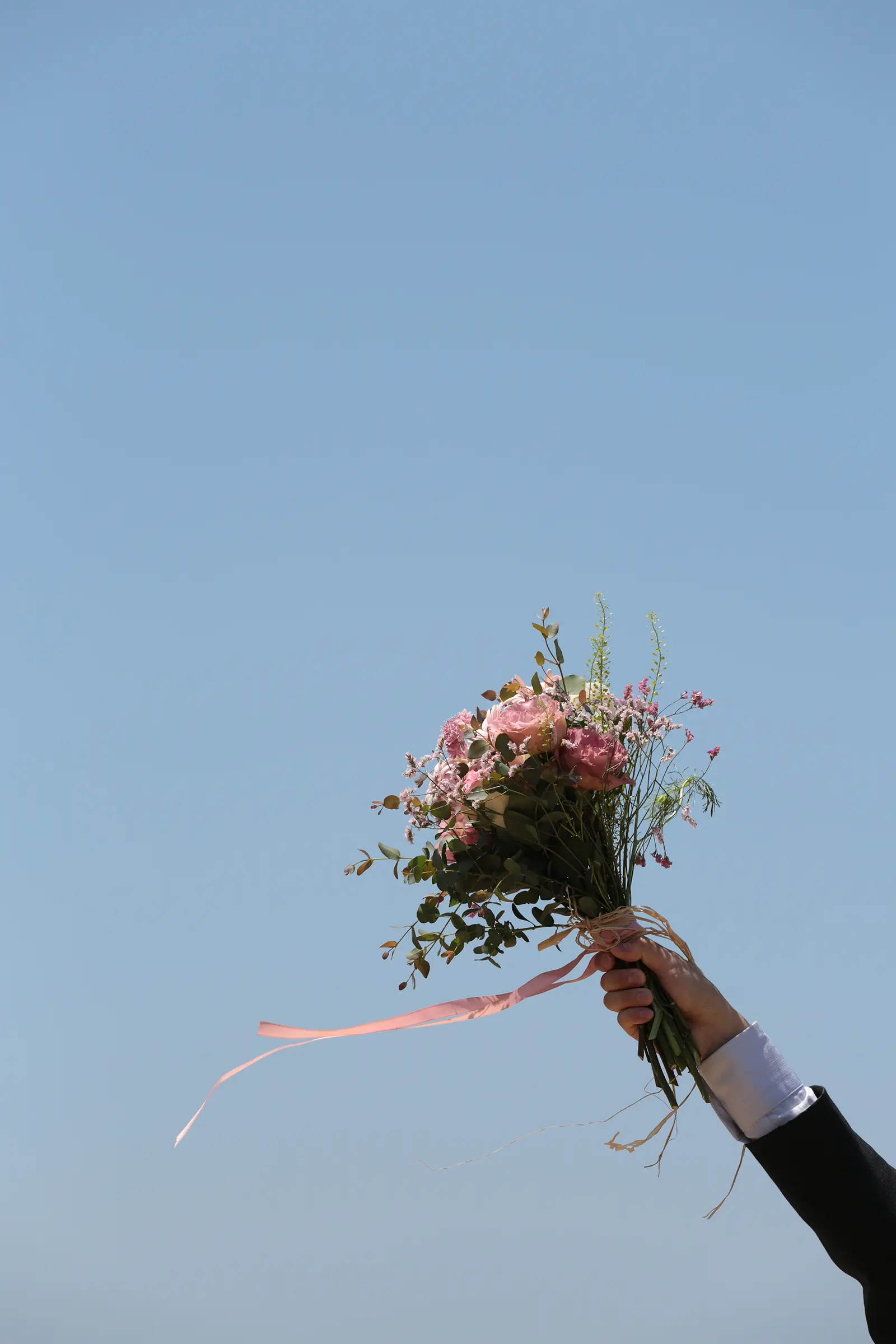 青空に向かってブーケを掲げるフォトウェディング写真