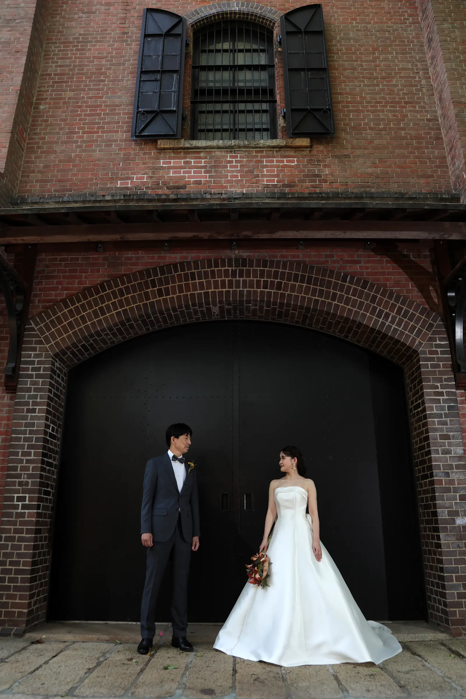 赤レンガの建物の前で向かい合う新郎新婦