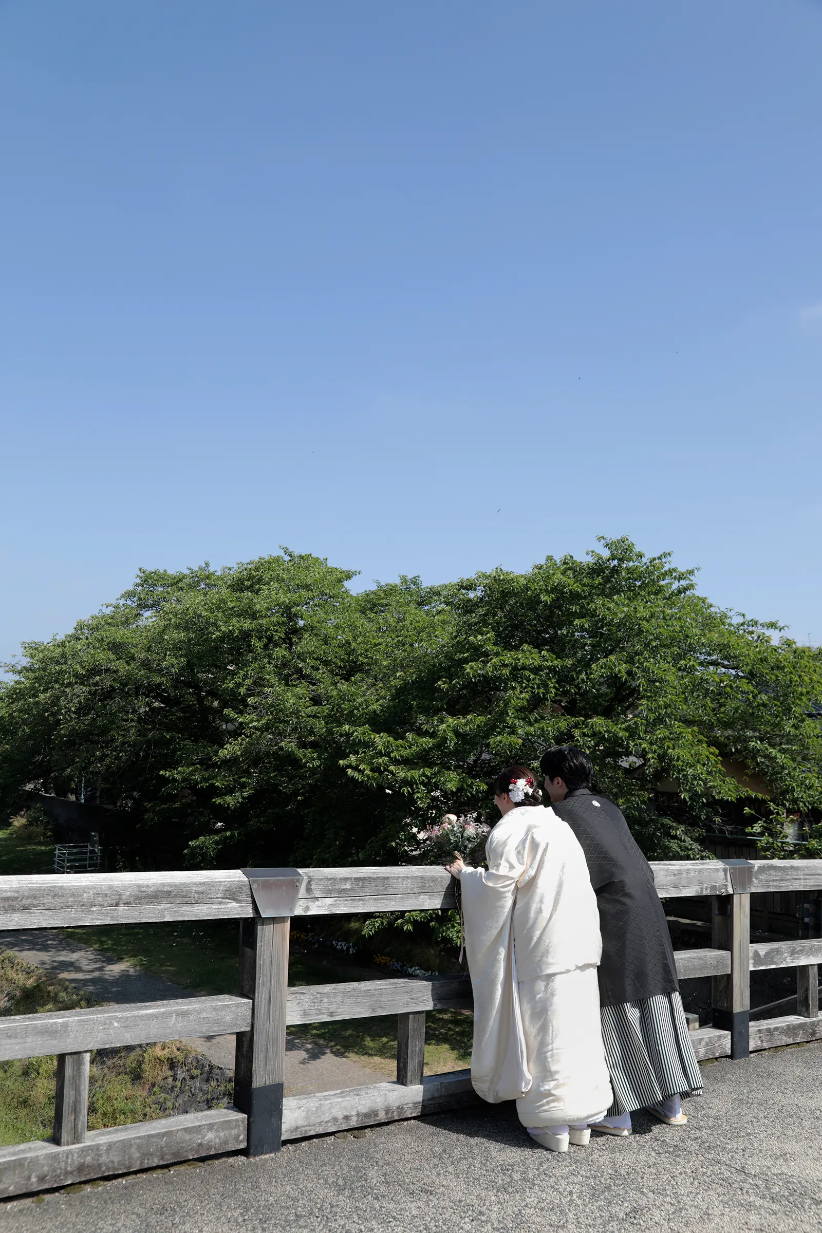 橋の欄干から景色を眺める和装の新郎新婦の後ろ姿