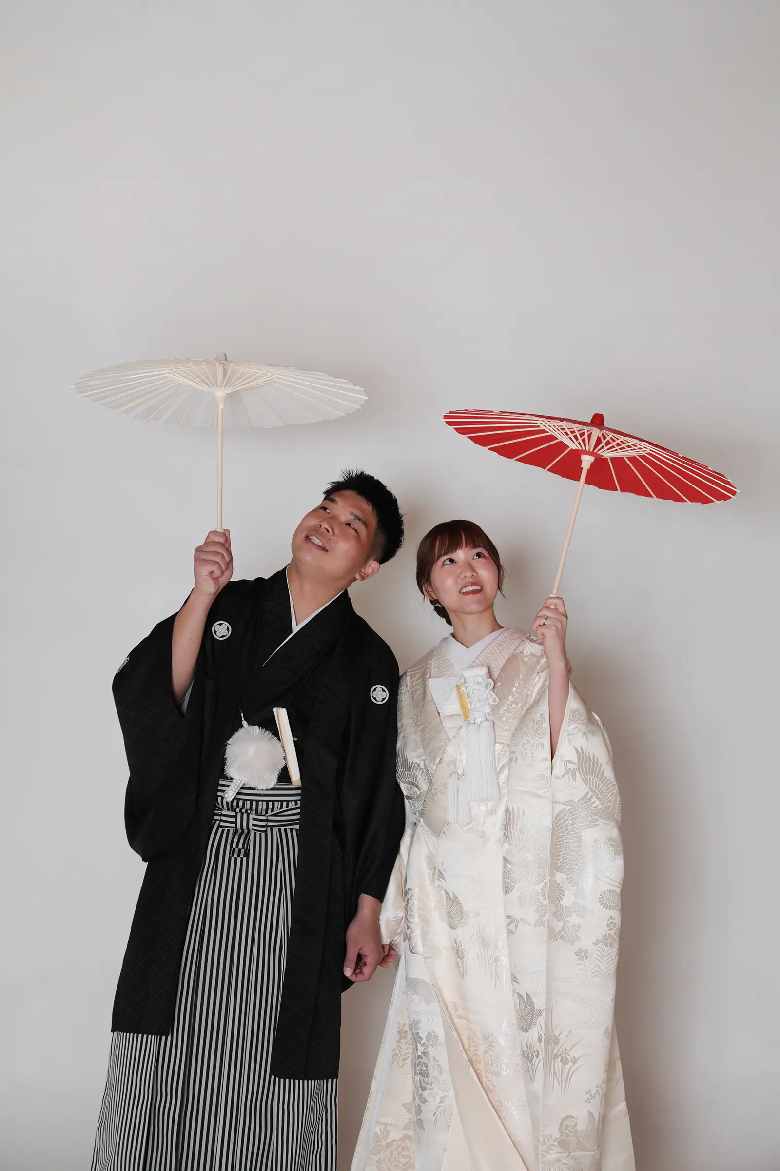 白背景の前で和傘を持つ和装の新郎新婦