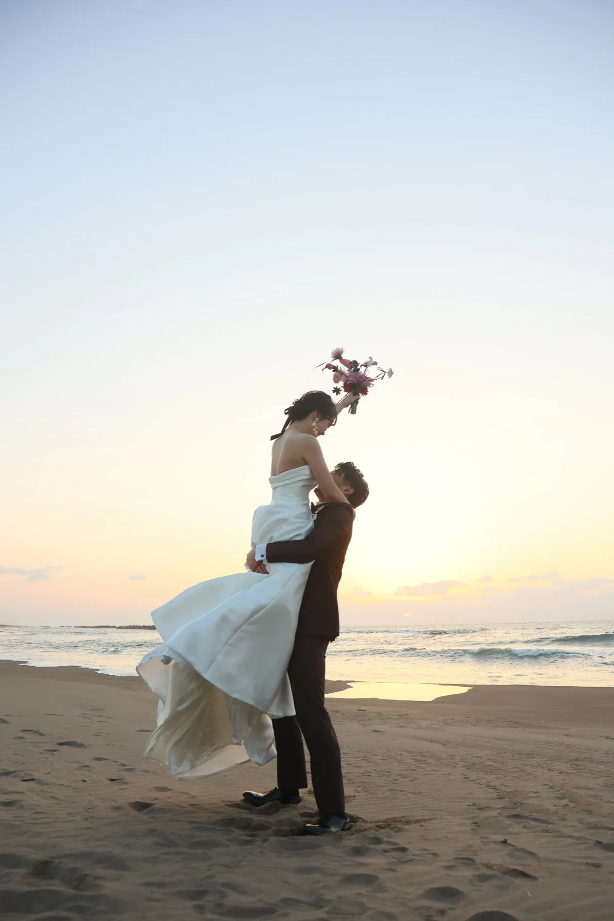 夕日の海辺で新婦を抱き上げる新郎、金沢のエモい洋装ロケーションフォトウェディング