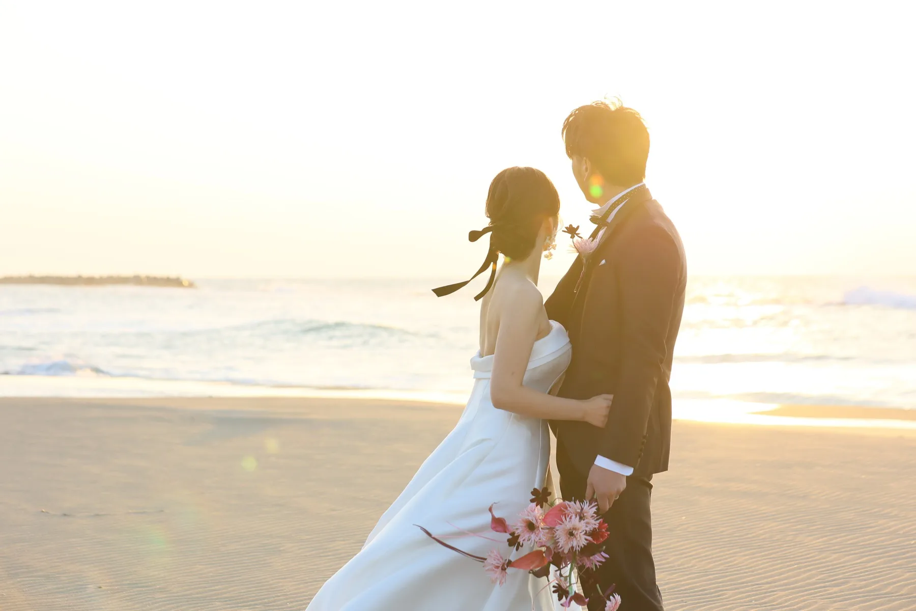 金沢の海辺で夕日を背景に寄り添う新郎新婦、洋装フォトウェディングのロケーション撮影