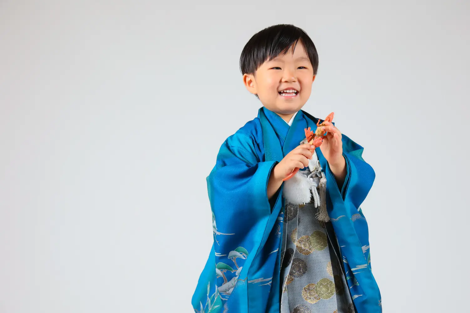 恐竜のおもちゃを両手に持って大笑いする5歳の男の子、青い羽織袴の七五三スタジオ撮影（金沢店）