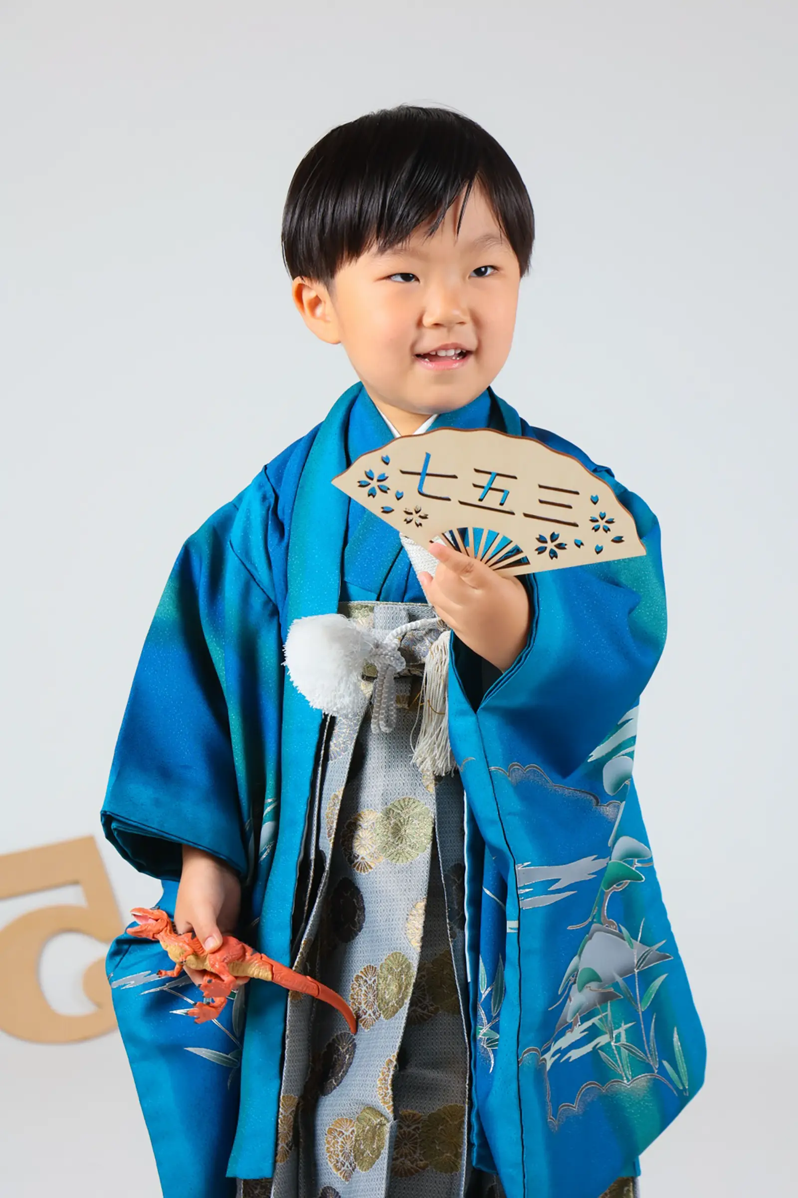 「七五三」と抜かれた扇形の木の小物を掲げる5歳の男の子、青い羽織袴の七五三スタジオ撮影（金沢店）