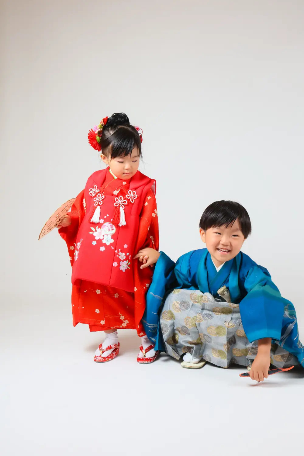 床の恐竜のおもちゃに手を伸ばす5歳の男の子と見守る3歳の女の子、七五三のスタジオ撮影（金沢店）