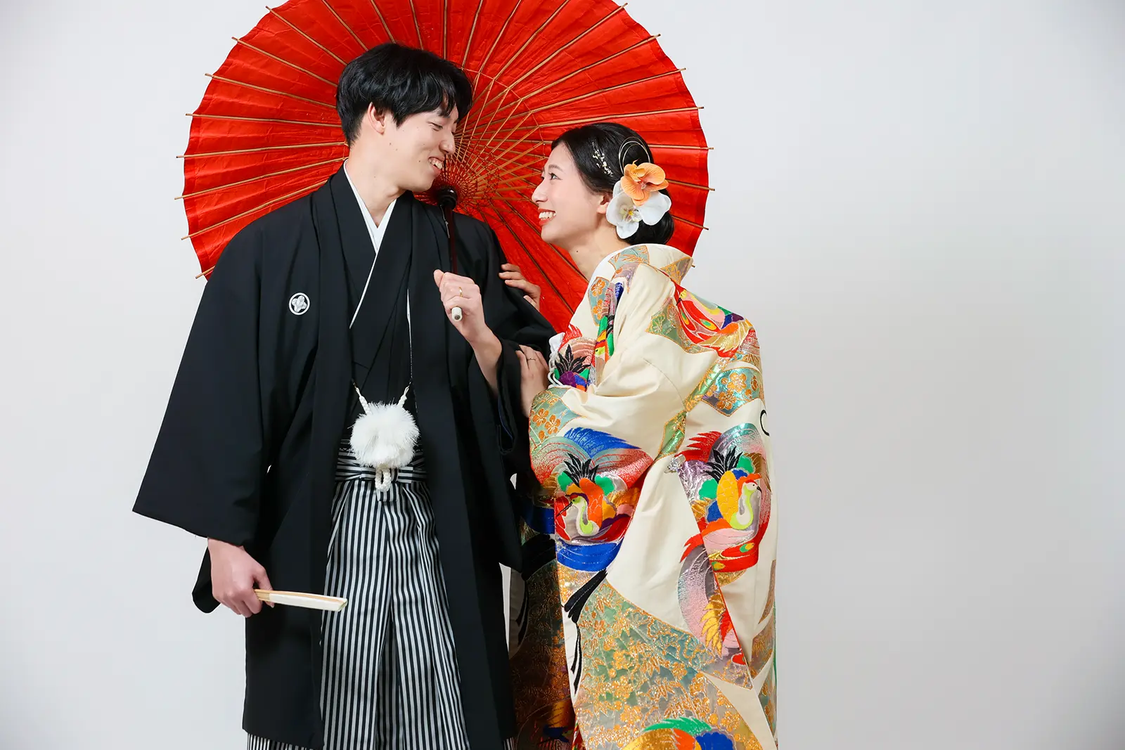 金沢のスタジオで赤い和傘を背景に見つめ合う和装姿の新郎新婦