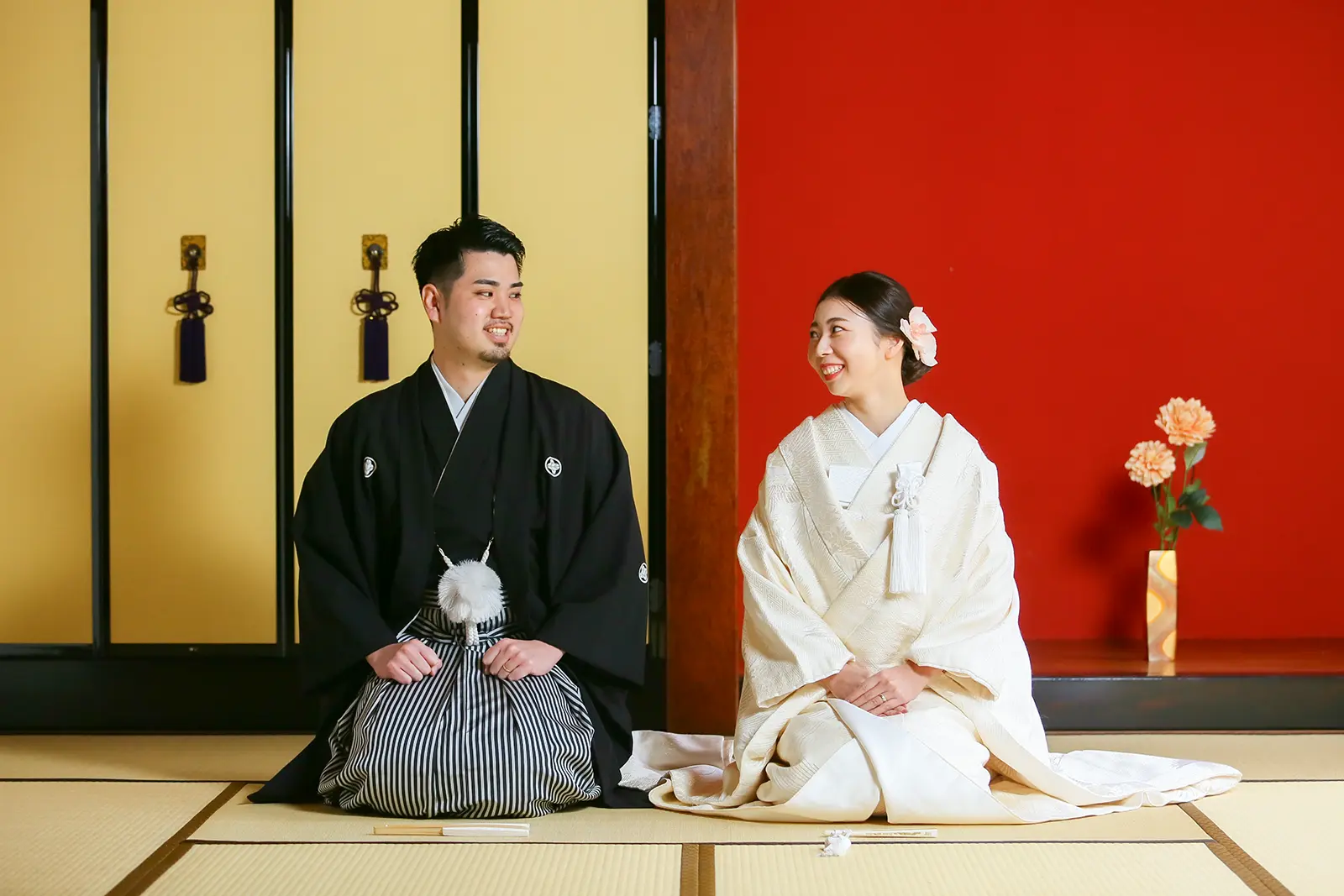 金沢のスタジオで赤い壁と金の襖を背景に座る和装姿の新郎新婦