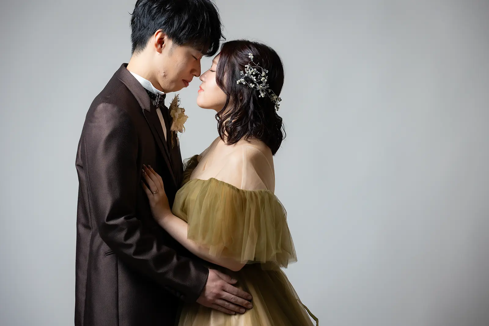 金沢のスタジオでブラウンタキシードとカーキカラーのドレス姿で寄り添う新郎新婦